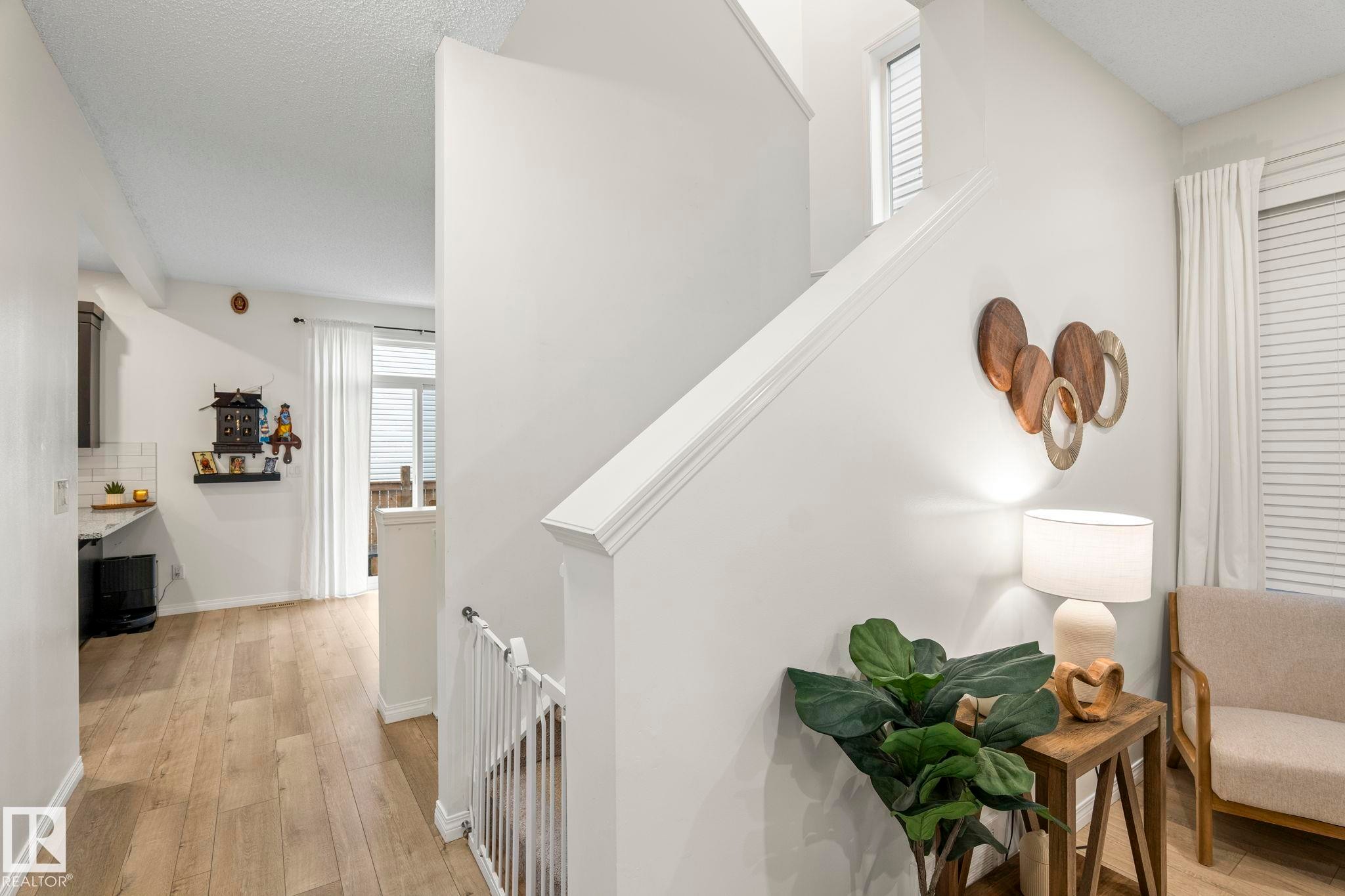 Staircase with white railing, light wood-finish flooring, white walls, and a window providing natural light - 20227 17Ave, Edmonton, AB