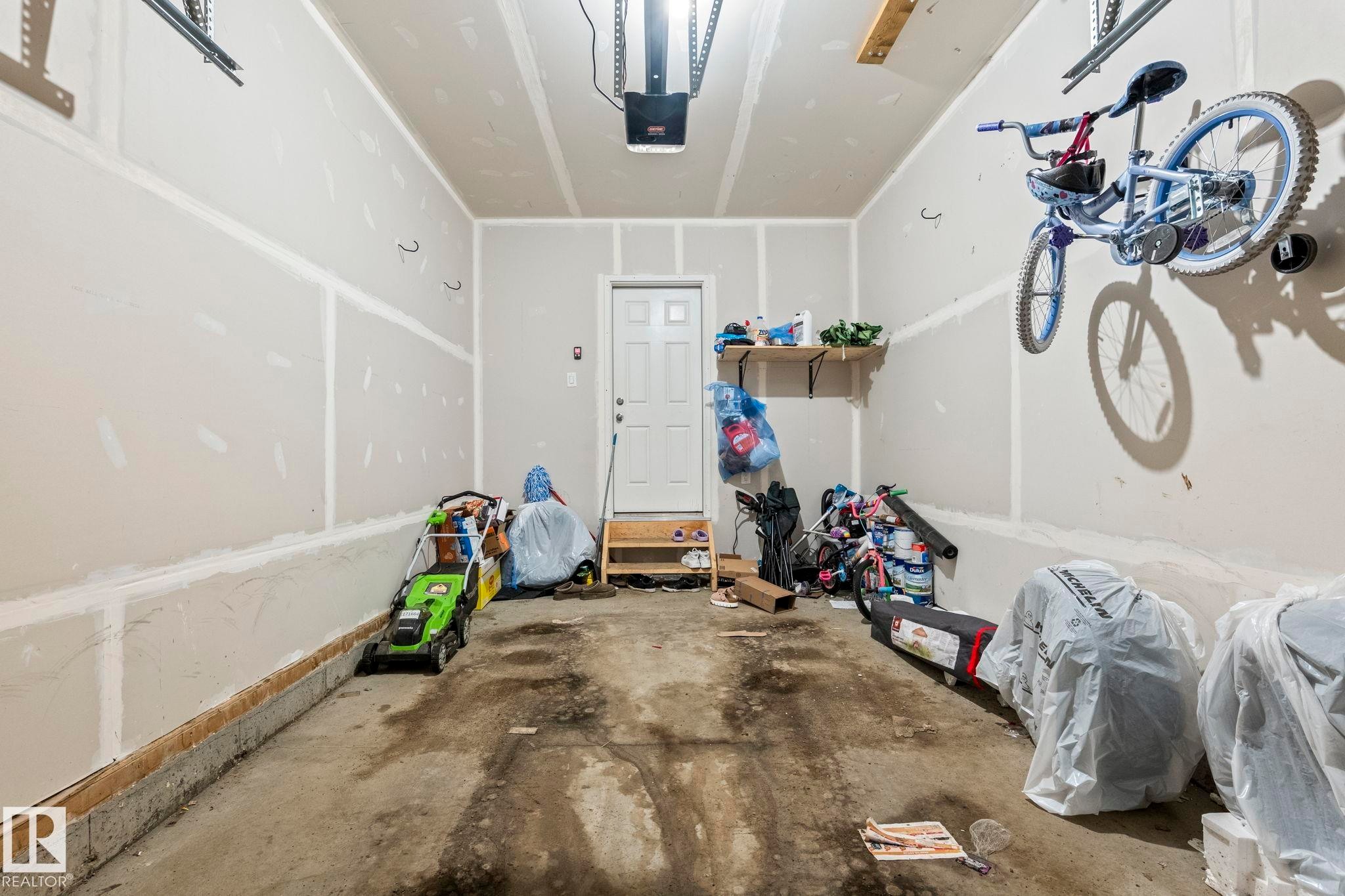 Spacious garage featuring a concrete floor, light gray walls, and an overhead garage door opener - 20227 17Ave, Edmonton, AB