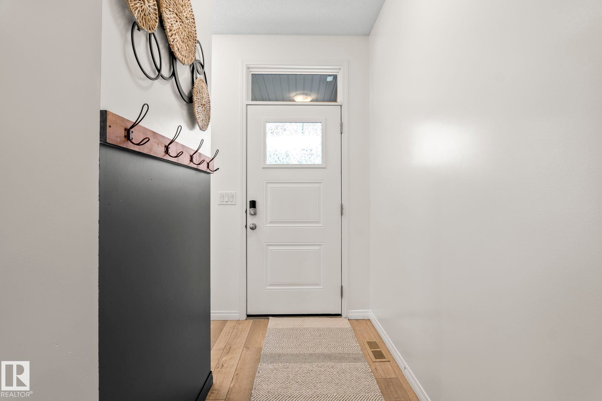 Entryway featuring wood-finish flooring and a white paneled door with frosted glass and a transom window - 20227 17Ave, Edmonton, AB
