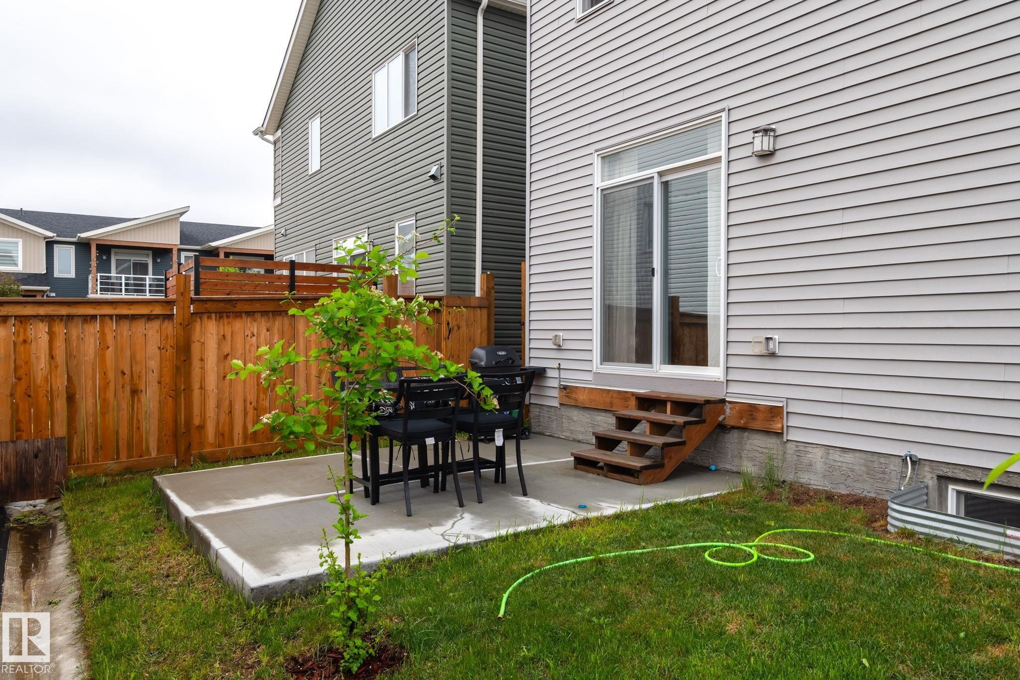 Concrete patio space with a wooden privacy fence and a small tree - 20227 17Ave, Edmonton, AB