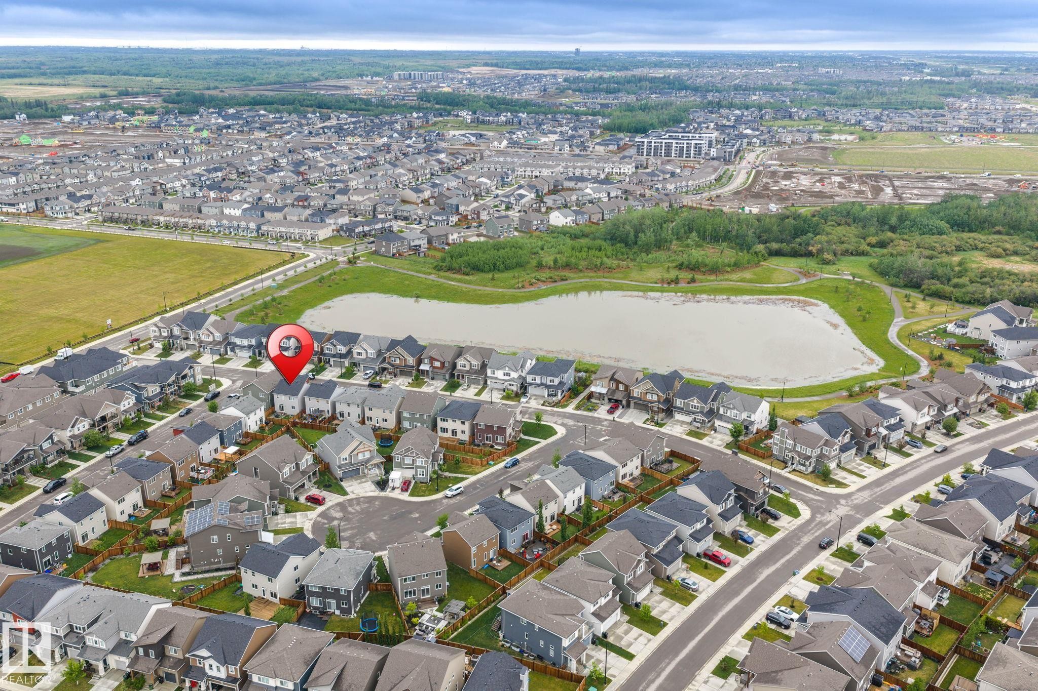 Aerial photograph showcasing a residential neighborhood with a large retention pond, surrounded by green spaces and a walking path - 20227 17Ave, Edmonton, AB