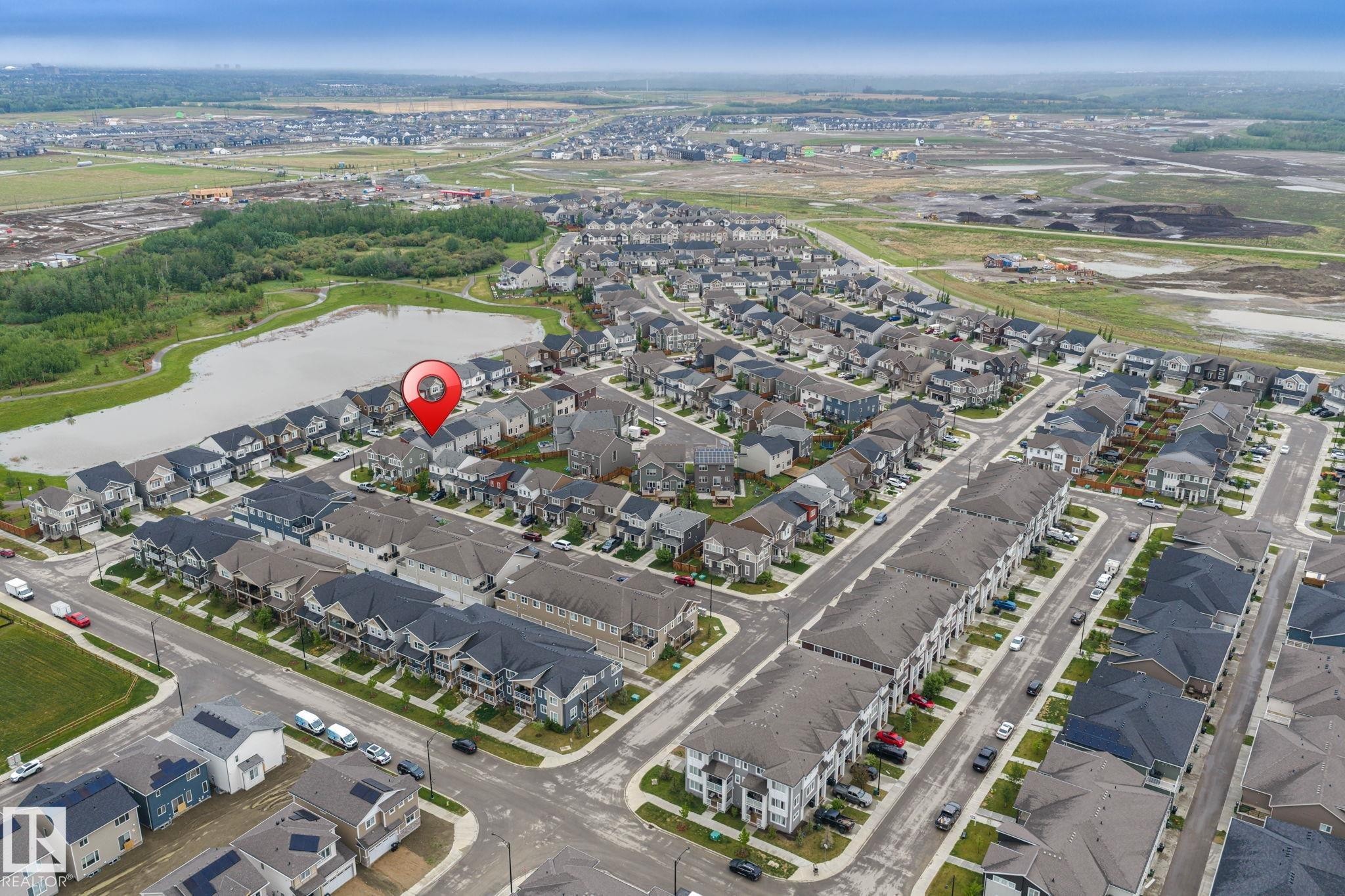 Aerial perspective showcasing a residential development with a prominent pond and green spaces - 20227 17Ave, Edmonton, AB