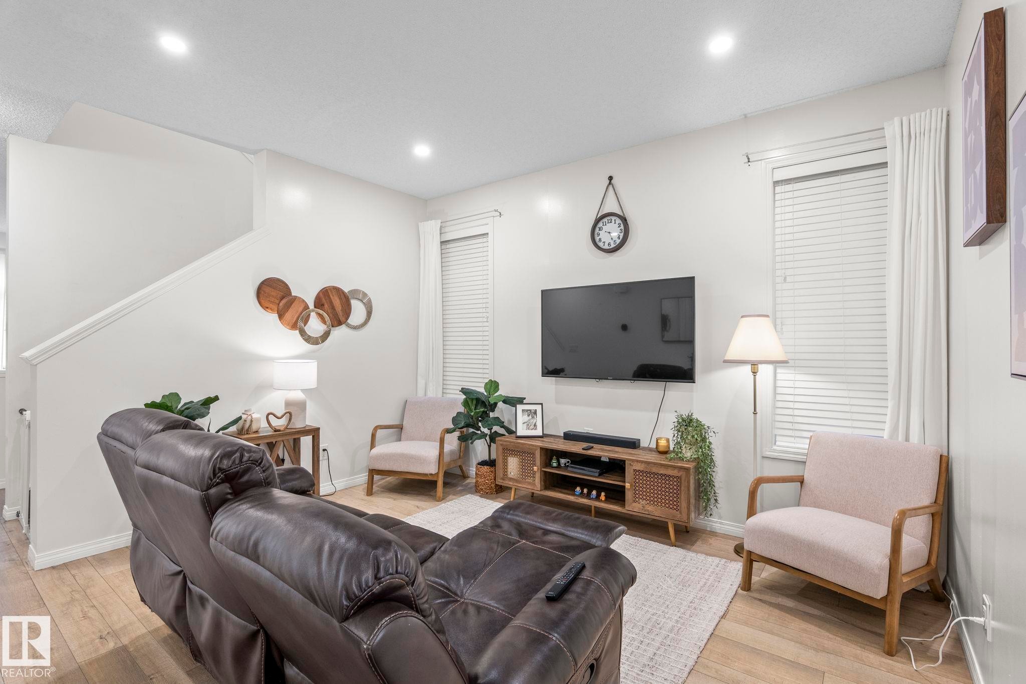 Spacious living area featuring wood-finish flooring, recessed lighting, and white window blinds - 20227 17Ave, Edmonton, AB