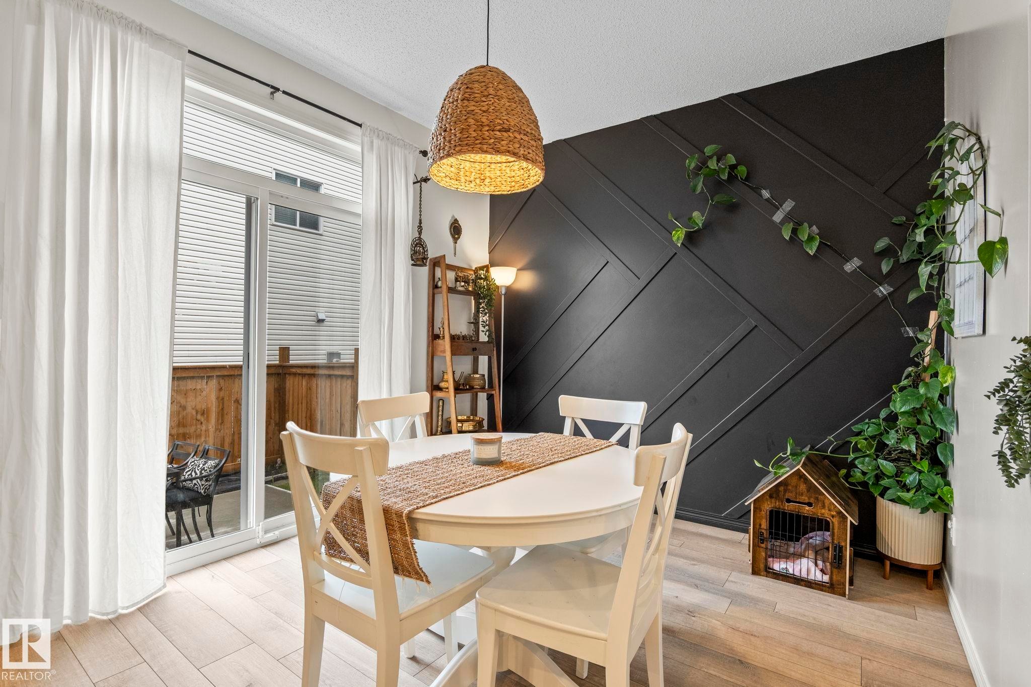Dining area featuring light wood-finish flooring, a contemporary black accent wall with geometric paneling, and a woven pendant light fixture - 20227 17Ave, Edmonton, AB