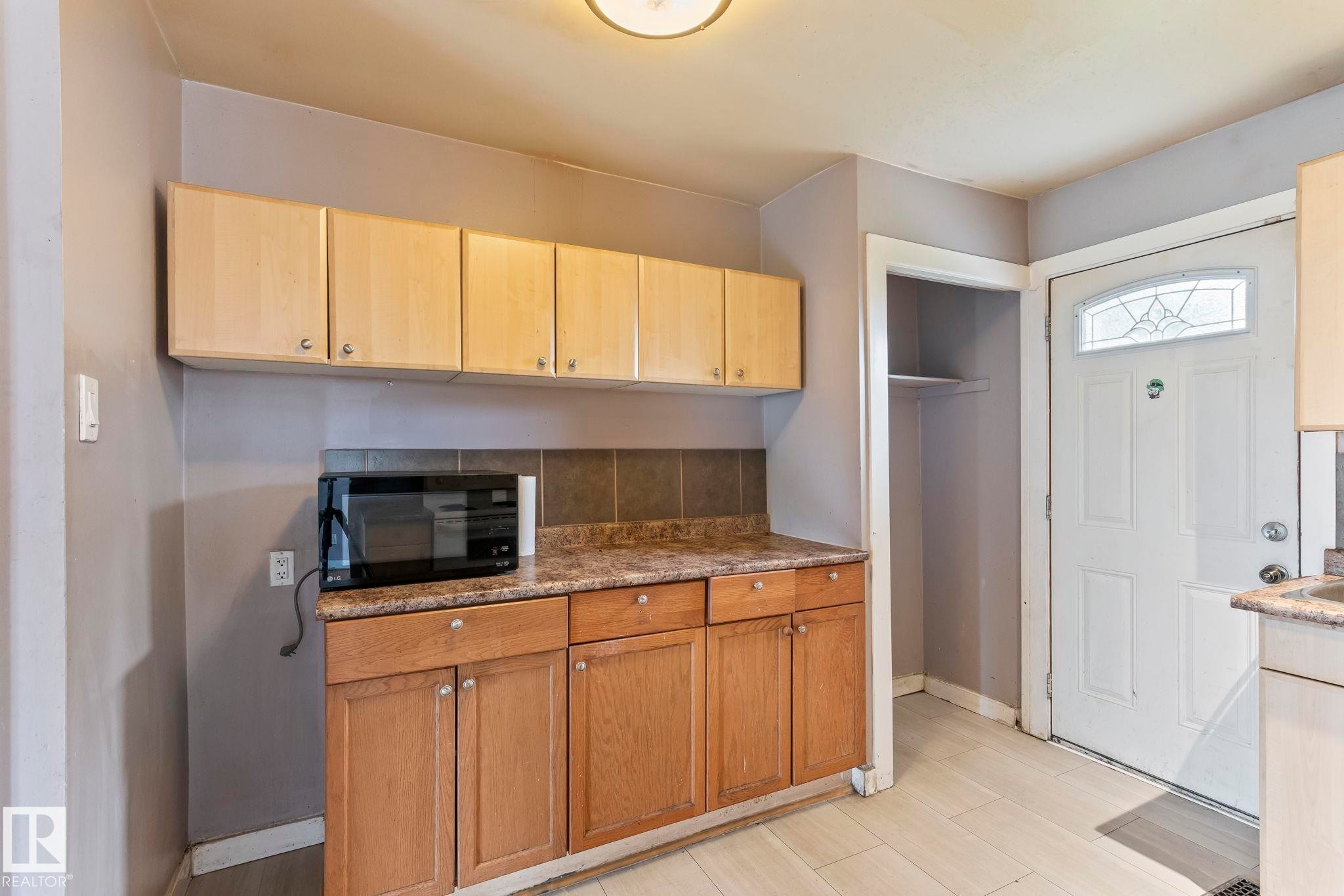 Kitchen area featuring wood-finish cabinetry, a laminate countertop, and a tile backsplash - 2045 46St, Edmonton, AB