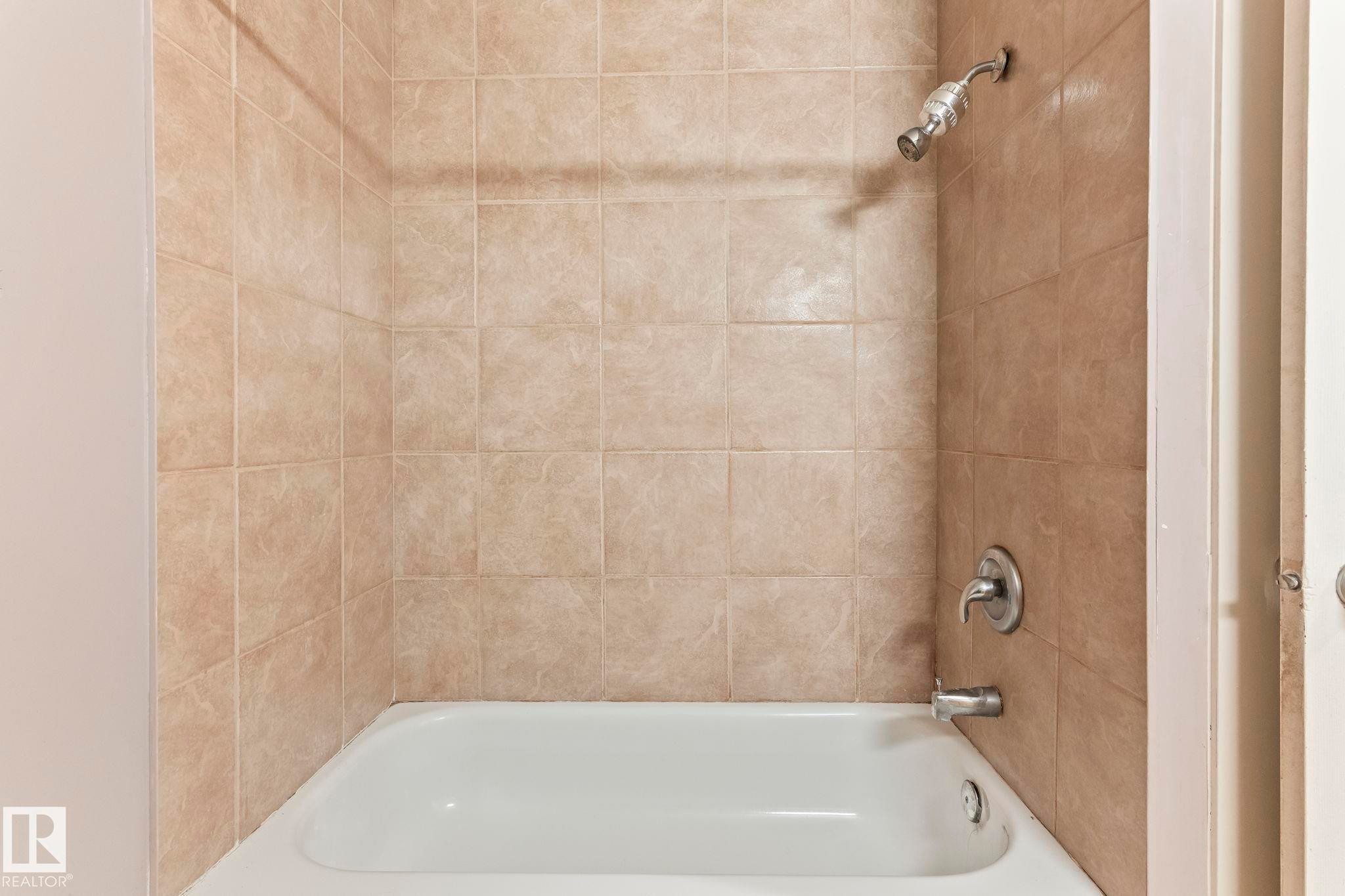White bathtub with light beige square wall tiling and chrome fixtures - 2045 46St, Edmonton, AB