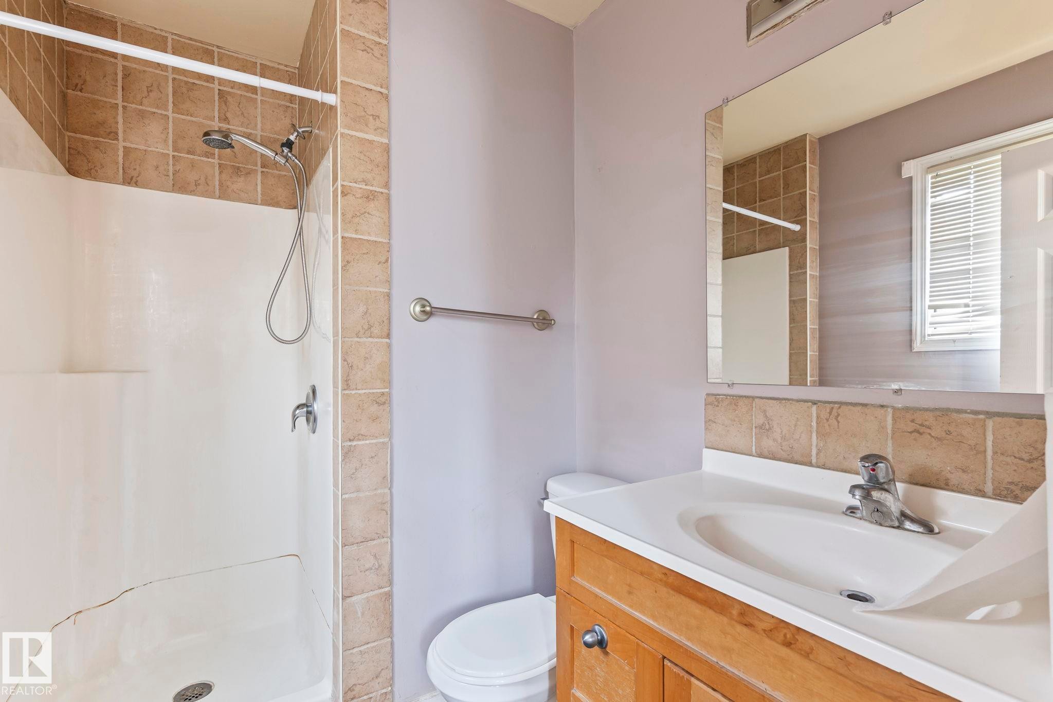 Bathroom with a tiled shower surround, integrated single-handle faucet, and a built-in wood-finish vanity with an integrated sink - 2045 46St, Edmonton, AB