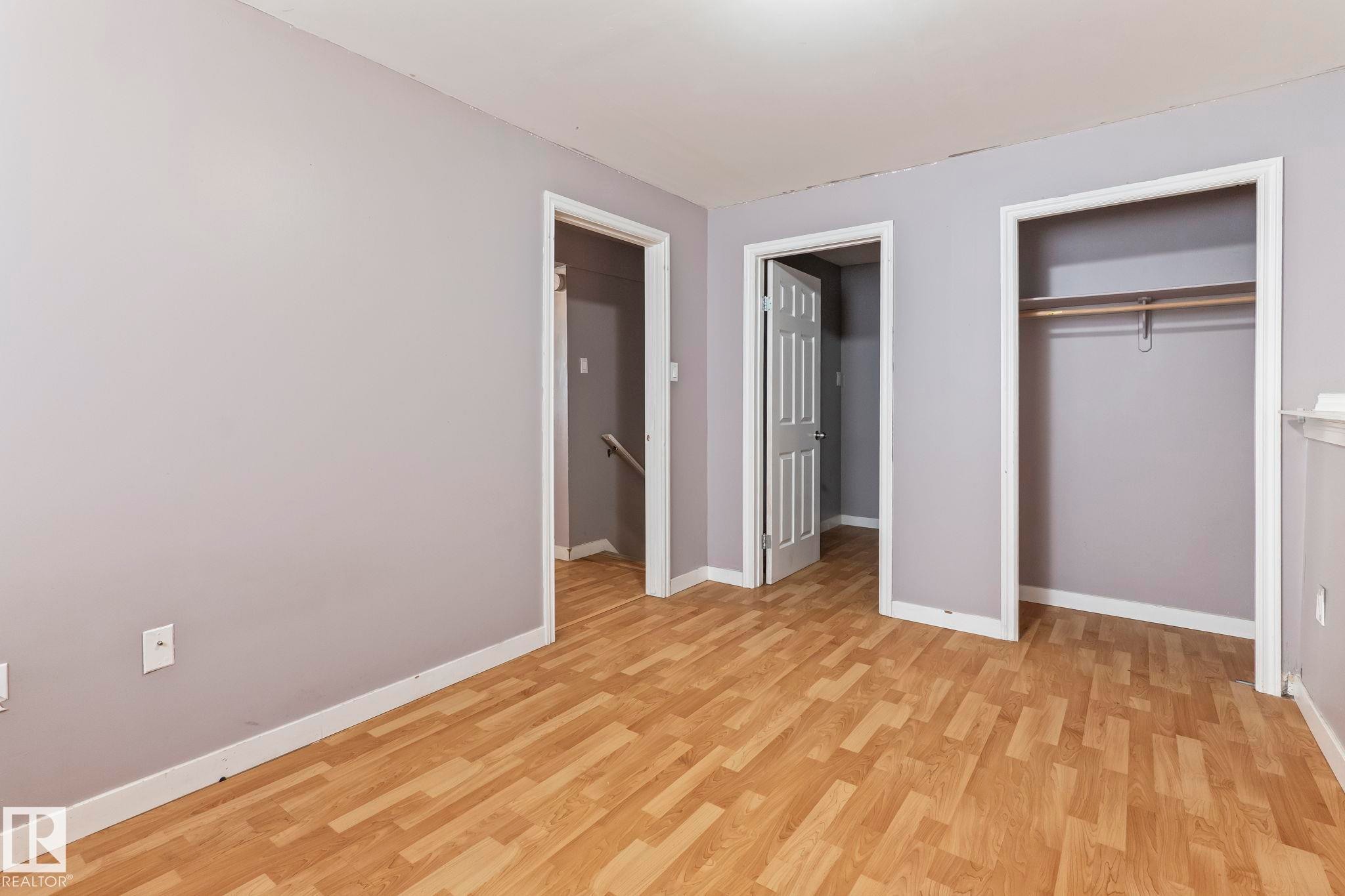 Spacious room featuring wood-finish flooring, light gray walls, white trim, and a built-in closet with shelving and hanging rod - 2045 46St, Edmonton, AB