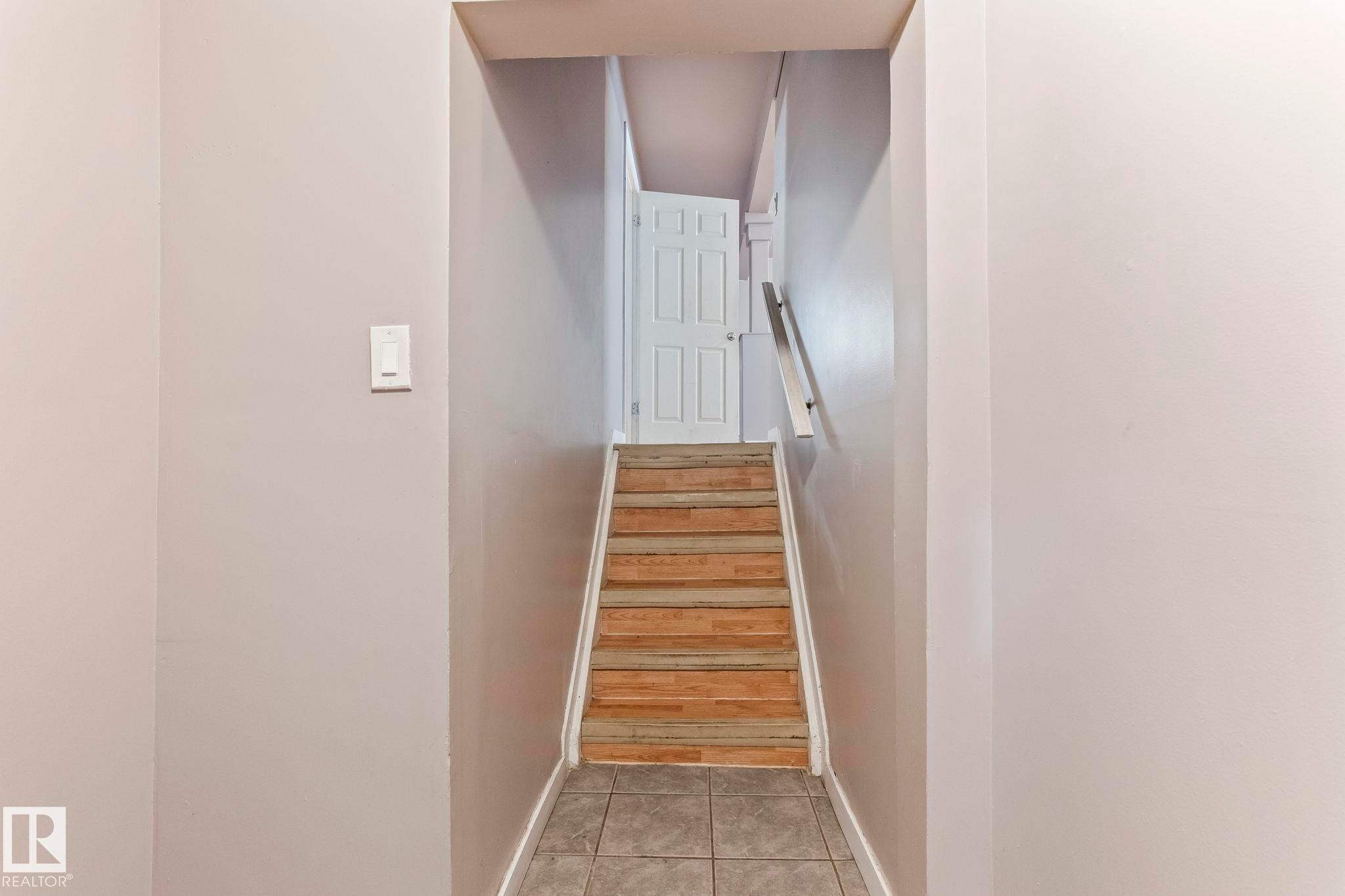 Staircase with wood-finish treads, a white handrail, and a paneled door at the landing - 2045 46St, Edmonton, AB