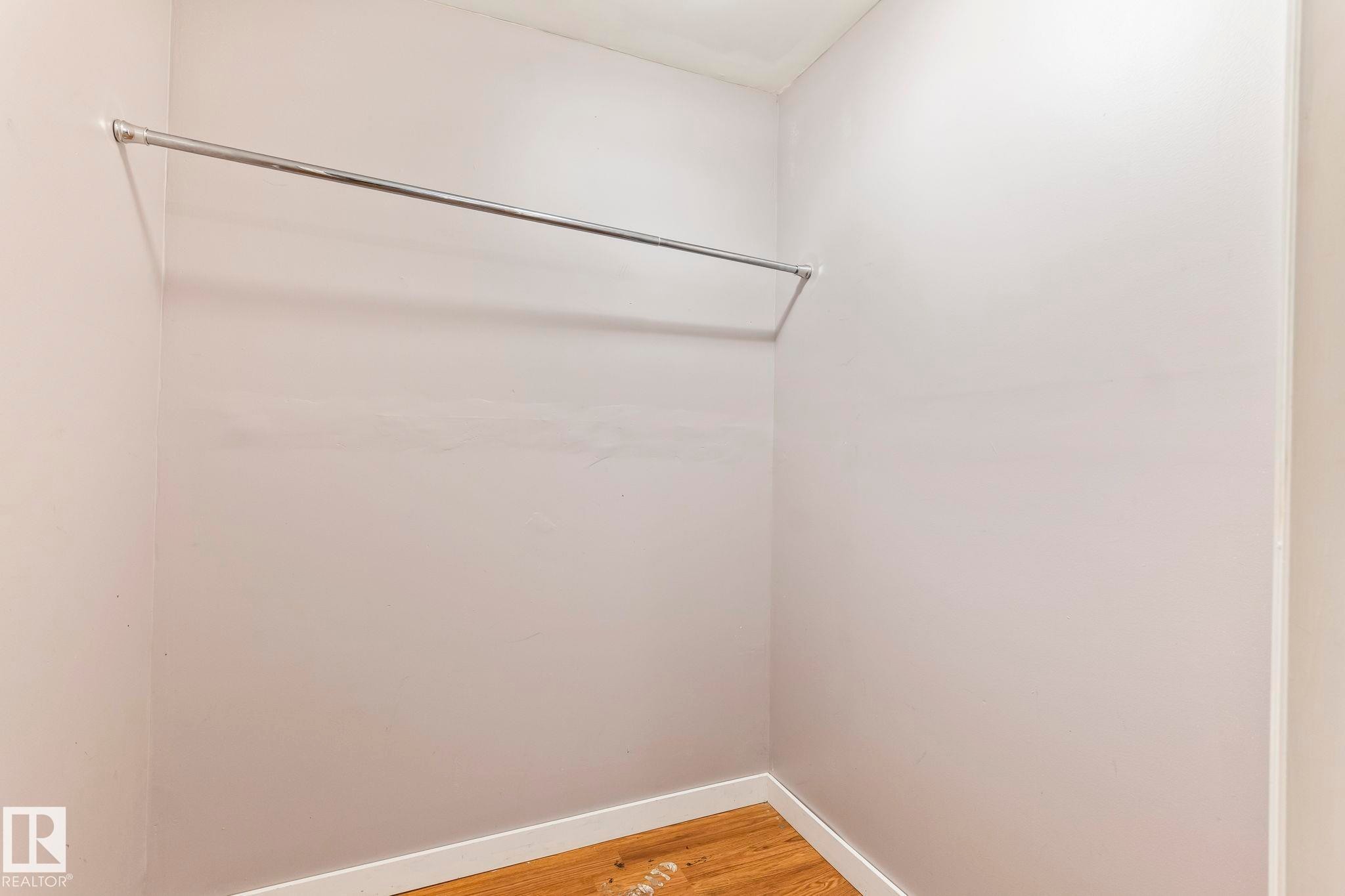 Walk-in closet featuring light-toned walls, wood-finish flooring, white baseboards, and an installed hanging rod - 2045 46St, Edmonton, AB