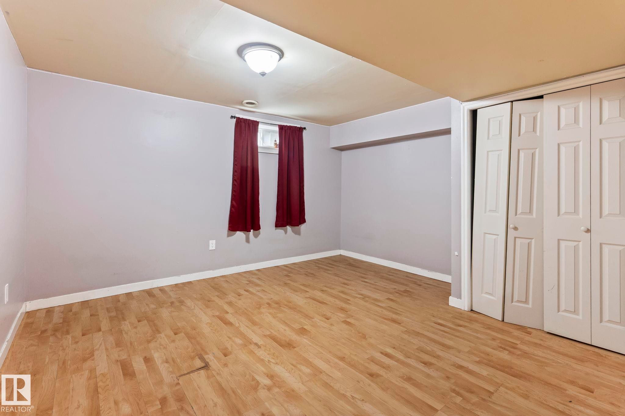Spacious room featuring wood-finish flooring, light grey walls, and a white ceiling - 2045 46St, Edmonton, AB