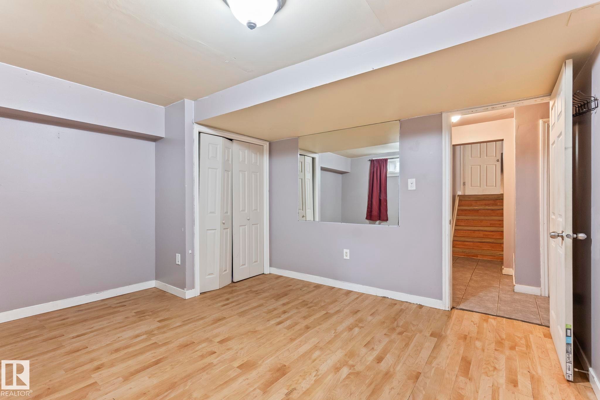 Spacious room featuring light wood-finish flooring, light purple wall paint, and white bi-fold closet doors - 2045 46St, Edmonton, AB