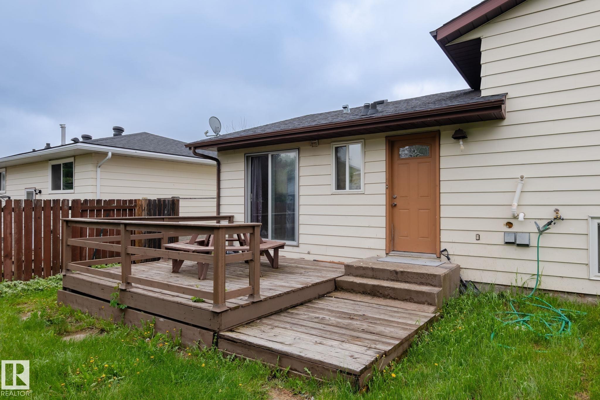 Rear exterior featuring a wooden deck with railing, sliding glass door, and an additional exterior door with a decorative glass insert - 2045 46St, Edmonton, AB