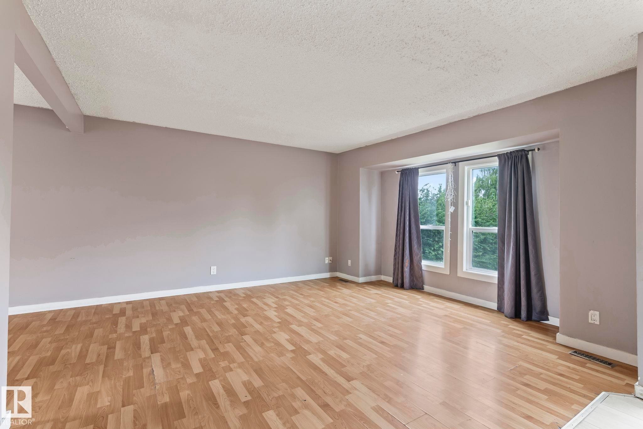 Spacious room featuring wood-finish flooring, light purple walls, and a large bay window - 2045 46St, Edmonton, AB