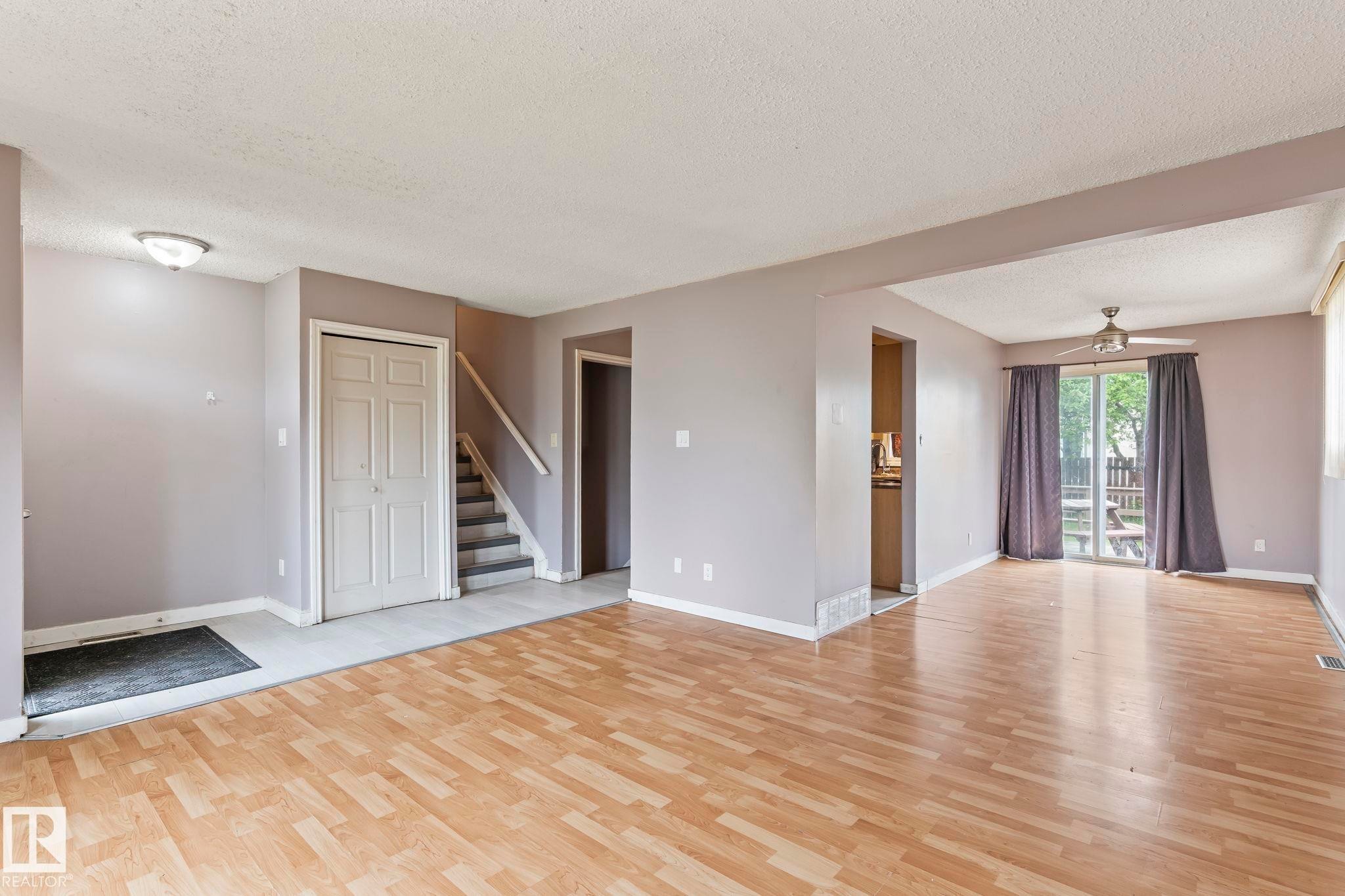 Open-concept living area with wood-finish flooring, a neutral color palette, and ample natural light from sliding glass doors - 2045 46St, Edmonton, AB