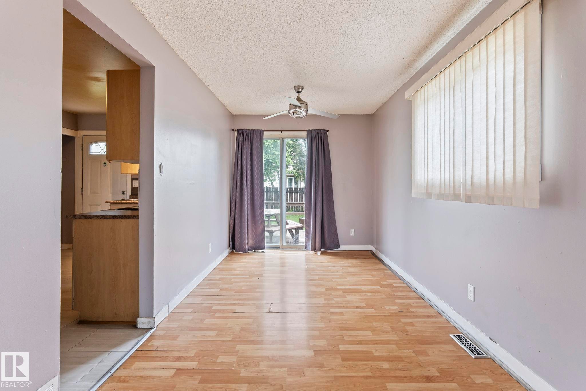 Spacious room featuring wood-finish flooring, a ceiling fan, and sliding glass doors leading to the outdoor space - 2045 46St, Edmonton, AB