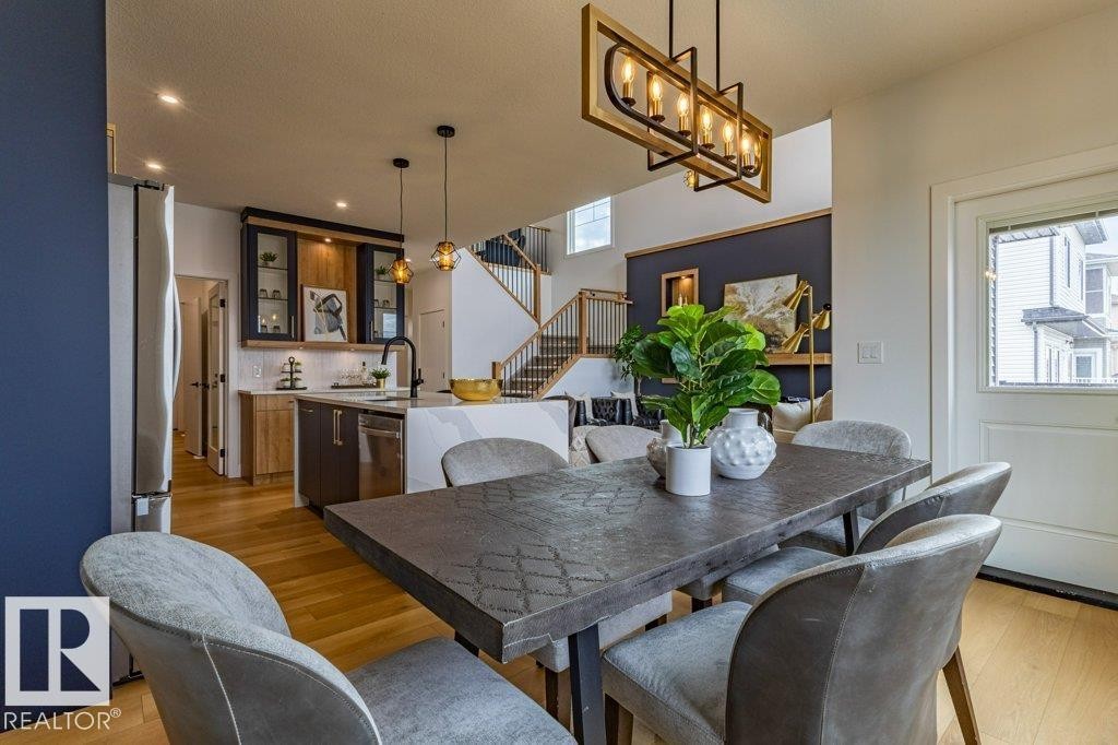 Open-concept living space featuring wood-finish flooring, a contemporary kitchen with stainless steel appliances, and a dining area with a modern chandelier - 82 Wynn Rd, Fort Saskatchewan, AB