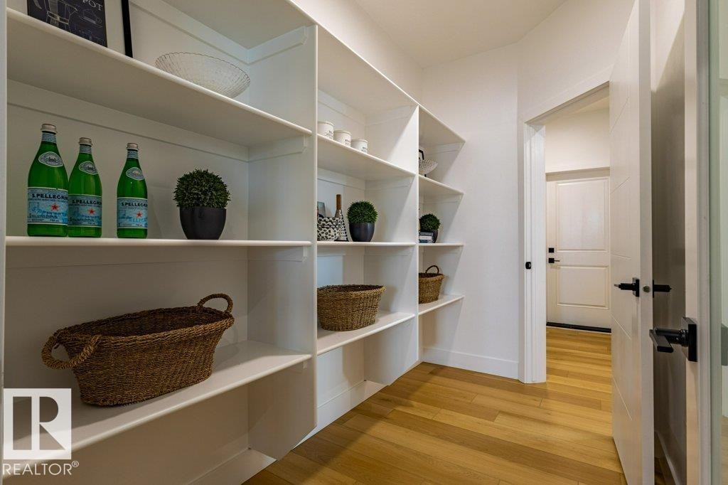 Built-in pantry shelving featuring white finishes, a solid core door with matte black hardware, and light wood-finish flooring - 82 Wynn Rd, Fort Saskatchewan, AB