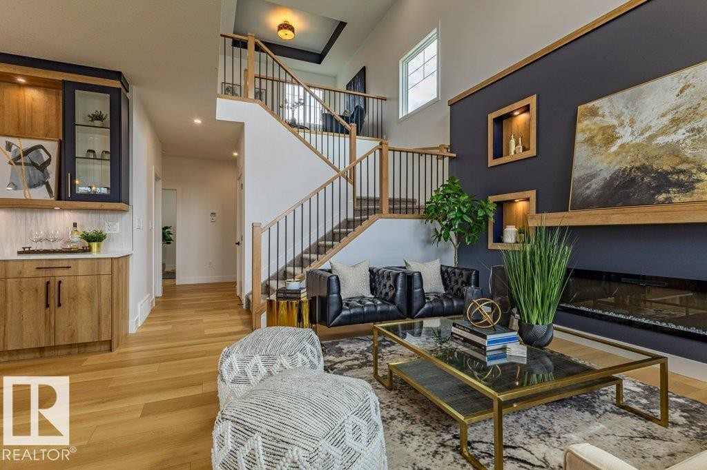 Open-concept living space featuring wood-finish flooring, a contemporary fireplace with a wood mantle, and a built-in wet bar with a curved countertop - 82 Wynn Rd, Fort Saskatchewan, AB