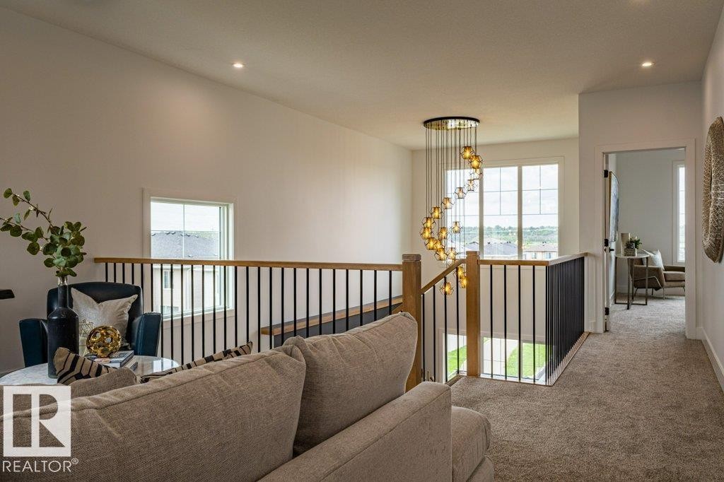 Upper-level landing featuring a contemporary spiral chandelier, wood-finish handrail with black metal balusters, and recessed lighting - 82 Wynn Rd, Fort Saskatchewan, AB