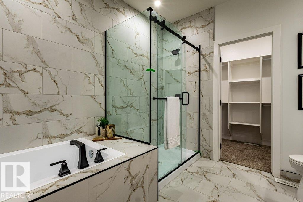 Bathroom featuring a built-in soaking tub with black fixtures, a walk-in shower with clear glass enclosure and black frame, extensive marble-look tile on walls and flooring, and an open closet with built-in shelving - 82 Wynn Rd, Fort Saskatchewan, AB