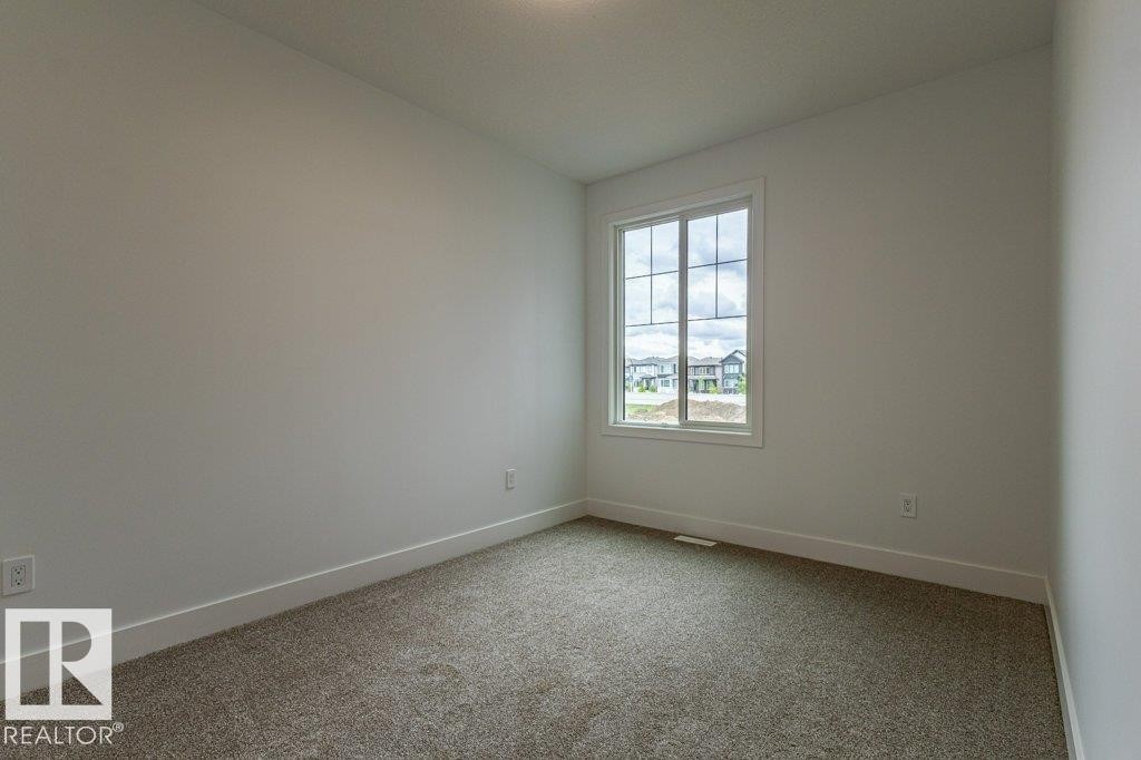 Room featuring a large window with white trim, gray carpet, white baseboards, and light-colored walls - 82 Wynn Rd, Fort Saskatchewan, AB