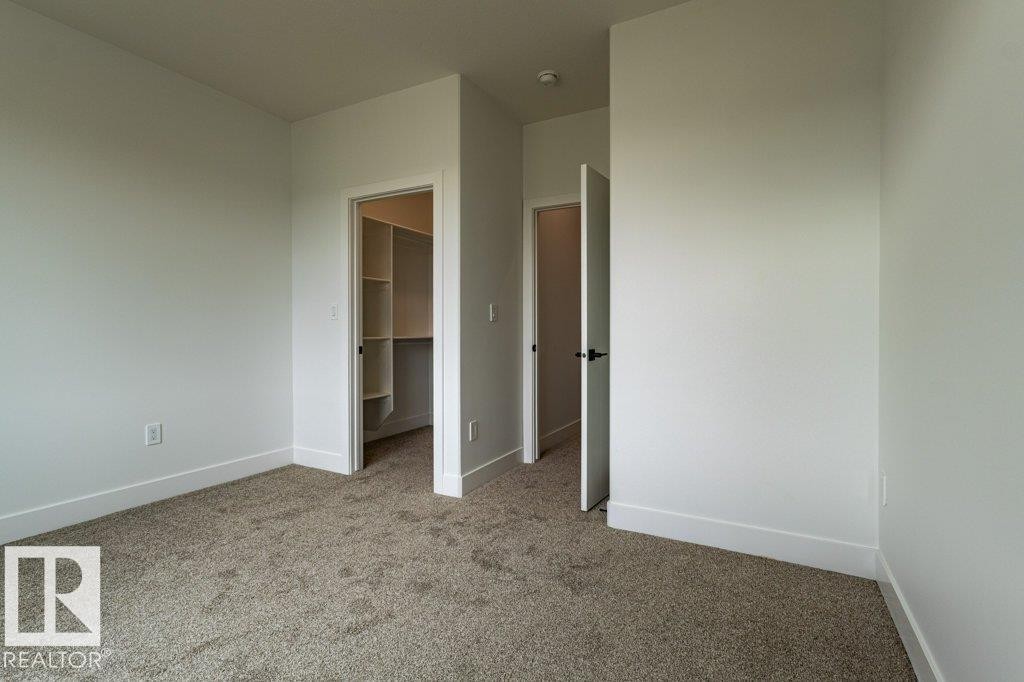Carpeted room featuring a walk-in closet with built-in shelving, white walls, white baseboards, and modern black door hardware - 82 Wynn Rd, Fort Saskatchewan, AB