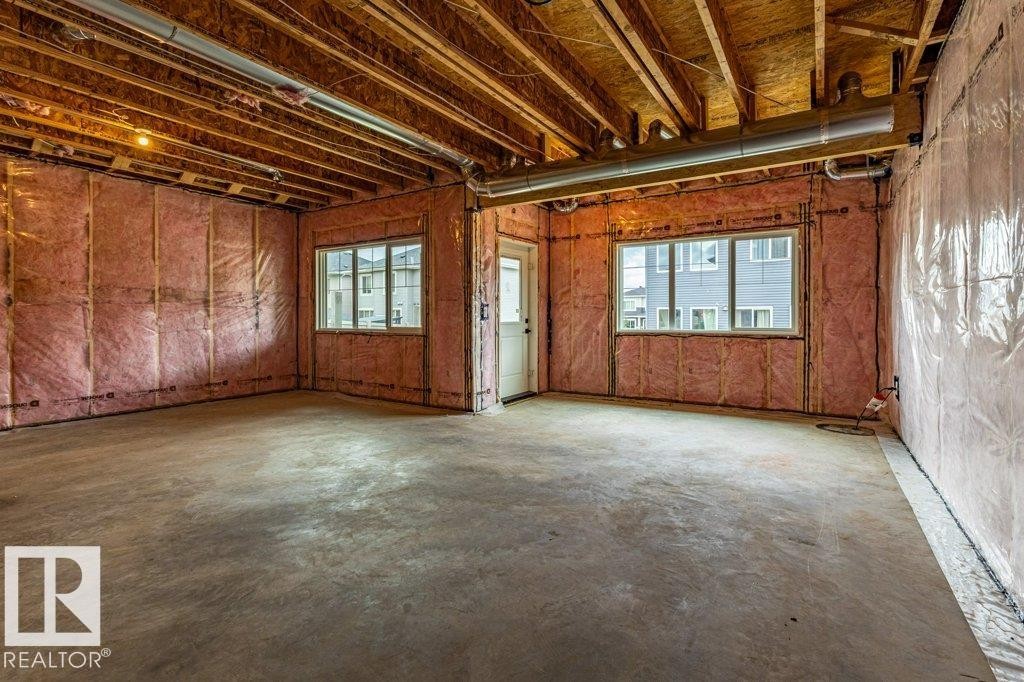 Unfinished basement featuring exposed wood joists, concrete flooring, two windows, insulated walls, and a white door frame - 82 Wynn Rd, Fort Saskatchewan, AB