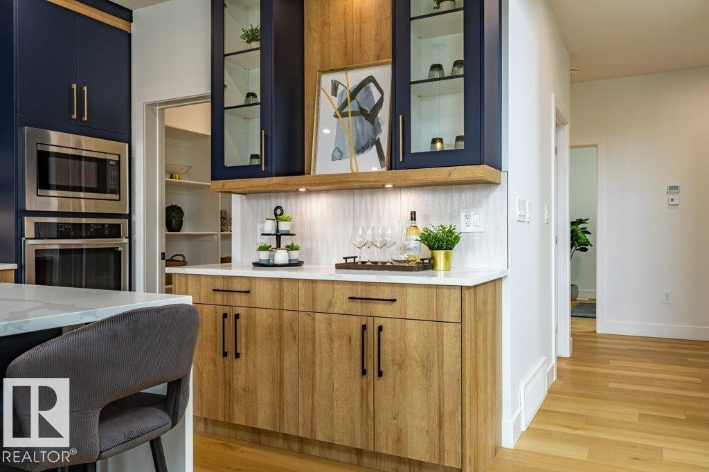 Kitchen featuring navy and wood-finish cabinetry, built-in stainless steel appliances, a white quartz countertop, and a tiled backsplash - 82 Wynn Rd, Fort Saskatchewan, AB
