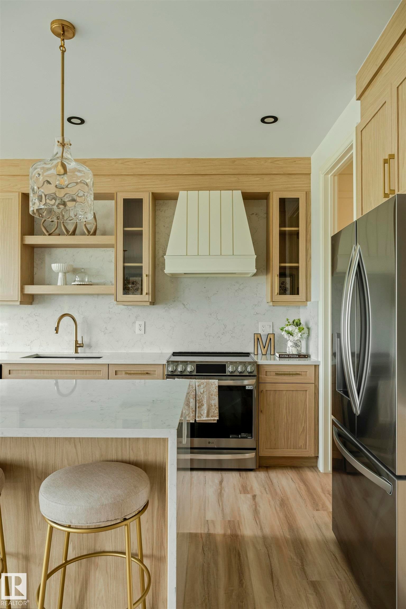 Modern kitchen featuring light wood-finish cabinetry, a stainless steel range with a custom range hood, and light-toned countertops - 3329 Chickadee Drive, Edmonton, AB