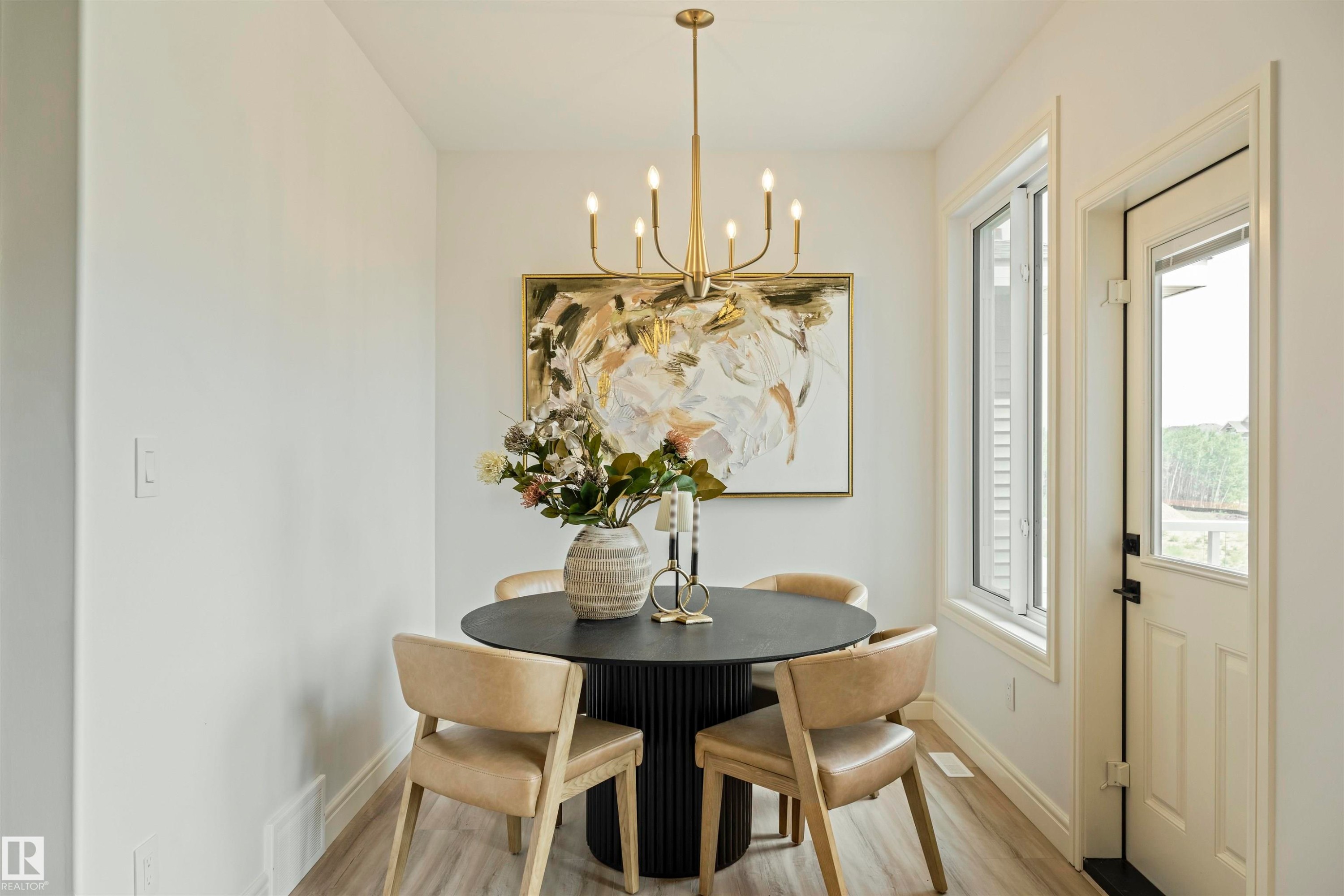 Dining area featuring a contemporary chandelier, light wood-finish flooring, and a glass-paneled exterior door - 3329 Chickadee Drive, Edmonton, AB