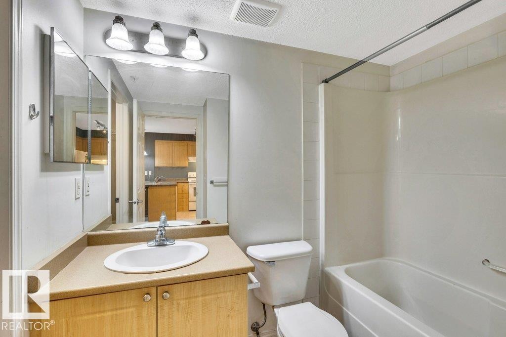 Bathroom featuring a wood-finish vanity with a beige countertop, a single basin sink, and a large mirror - 116 630 Mcallister Loop, Edmonton, AB