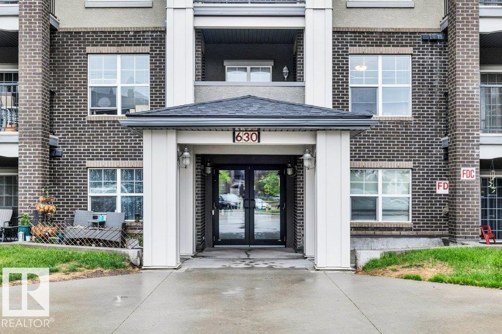 Building exterior featuring a covered entryway with a pitched roof, dark brick facade, and multiple windows - 116 630 Mcallister Loop, Edmonton, AB