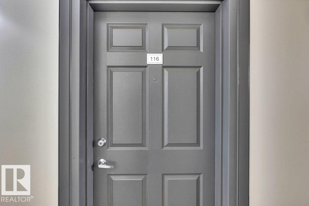 Panel-style entry door in a gray finish, featuring a silver-toned doorknob and lever handle - 116 630 Mcallister Loop, Edmonton, AB