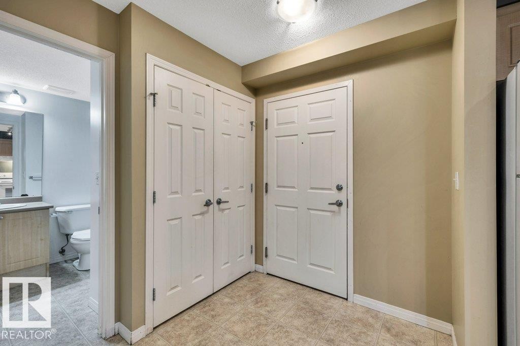 Entry area featuring a solid panel front door with brushed nickel hardware, neutral wall paint, and textured ceiling - 116 630 Mcallister Loop, Edmonton, AB