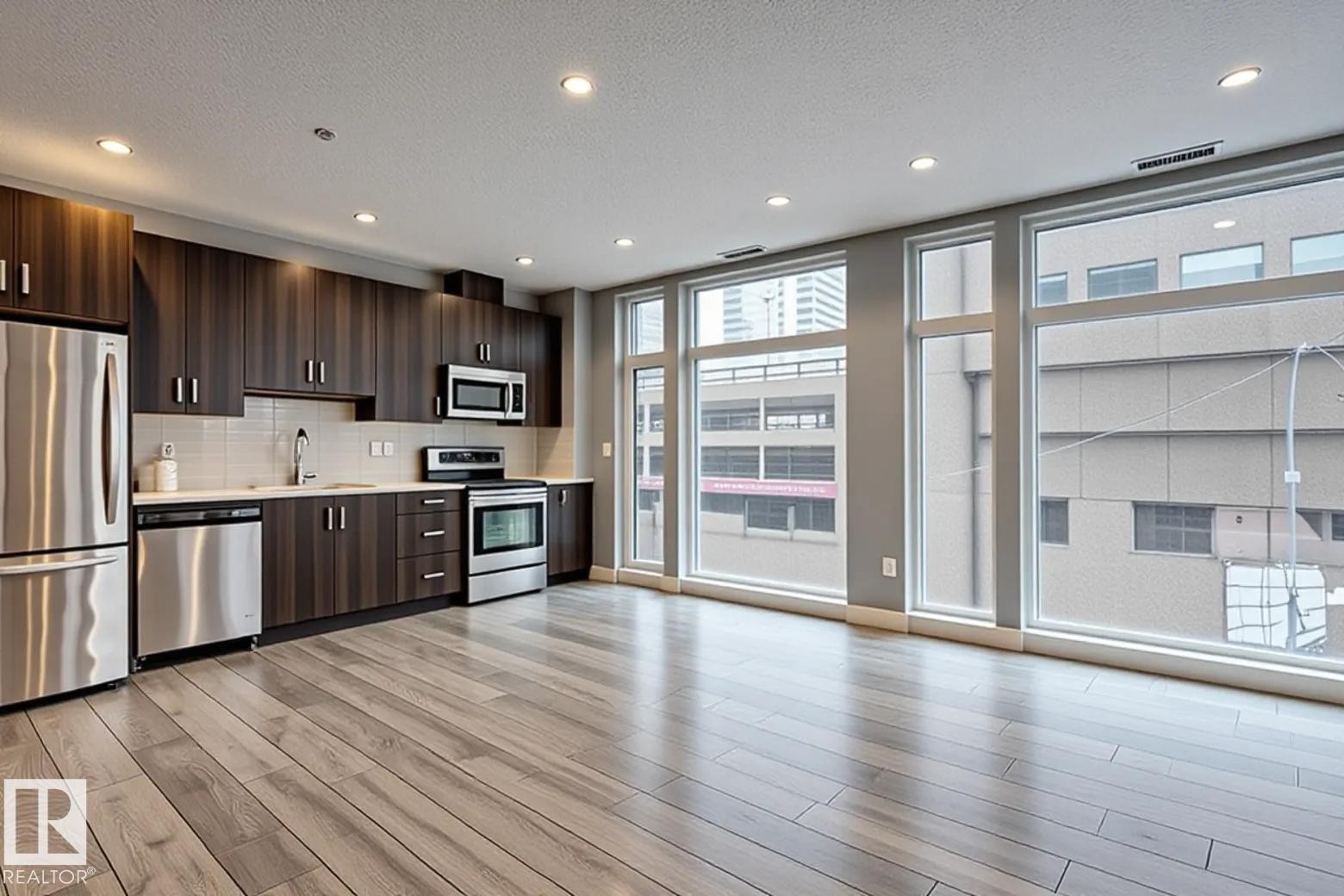 Open-concept kitchen and living area featuring wood-finish flooring, recessed lighting, and expansive windows - 401 10238 103 Street, Edmonton, AB - Indoor Photo Showing Kitchen With Stainless Steel Kitchen With Upgraded Kitchen