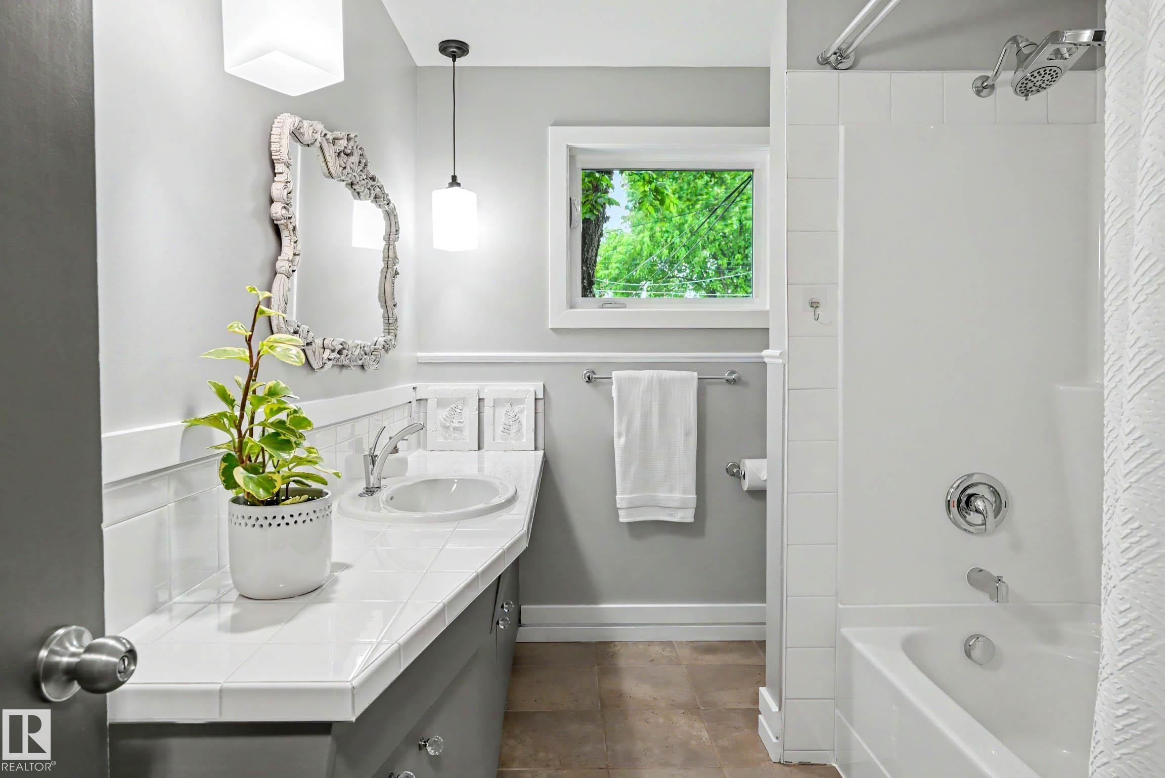Bathroom featuring a white tile vanity with an integrated sink, a deep soaking tub with a shower combination, and a decorative framed mirror - 12115 40 Avenue Nw, Edmonton, AB