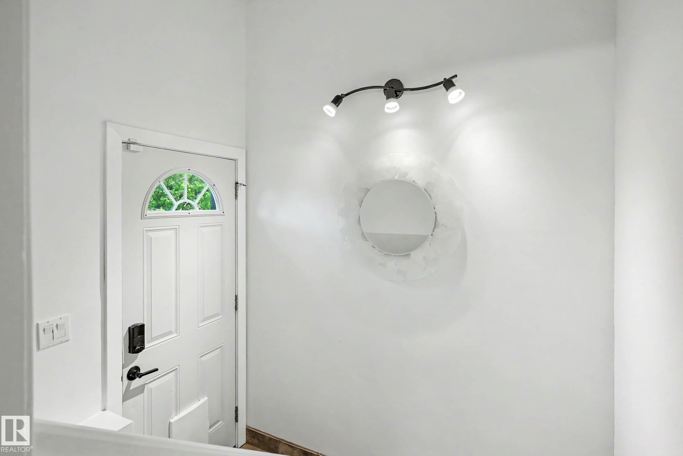 Entryway featuring a white paneled door with an arched transom window, contemporary track lighting, and a round wall mirror - 12115 40 Avenue Nw, Edmonton, AB