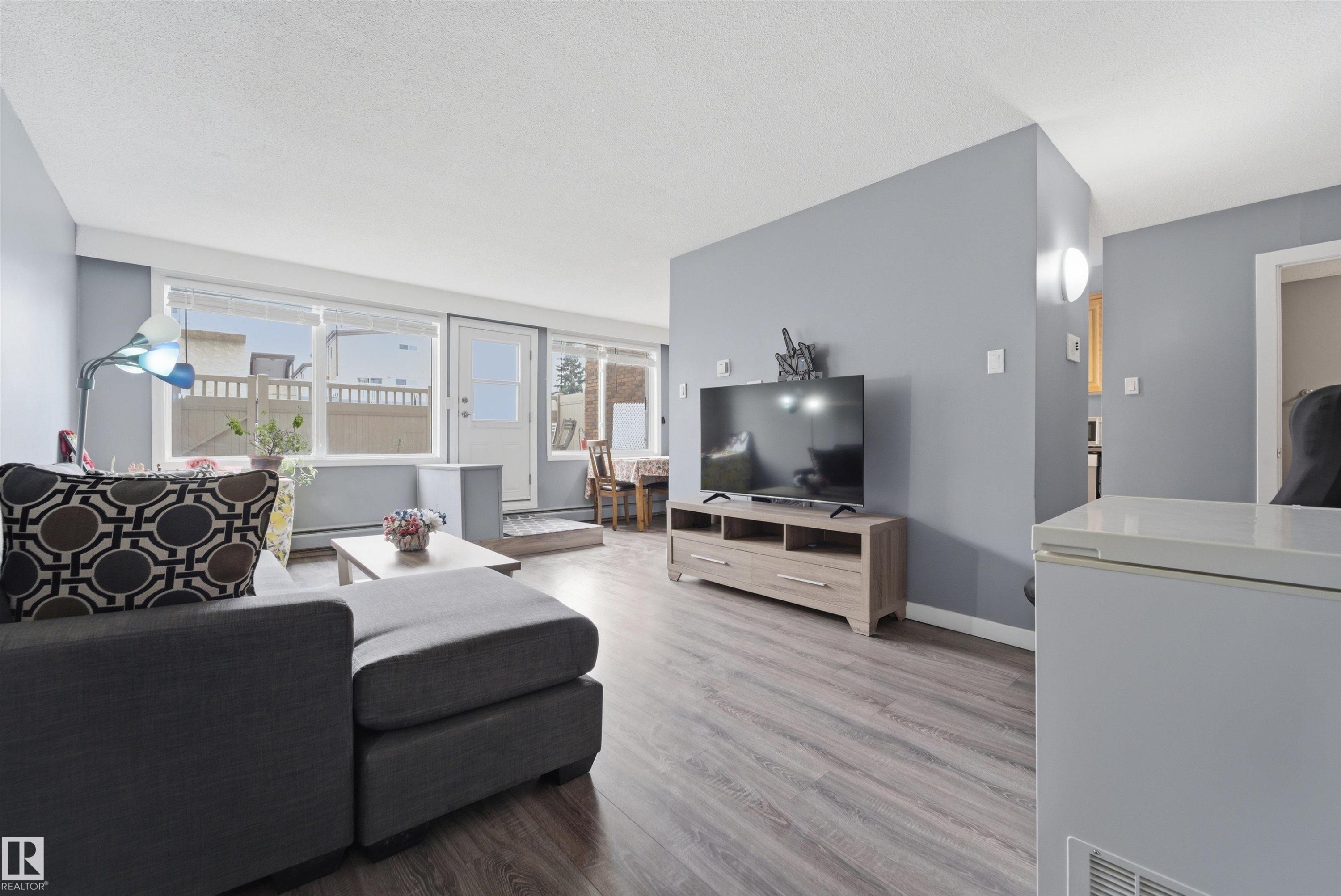 Spacious living area featuring light gray walls and wood-finish flooring - #110 7805 159 St Nw, Edmonton, AB