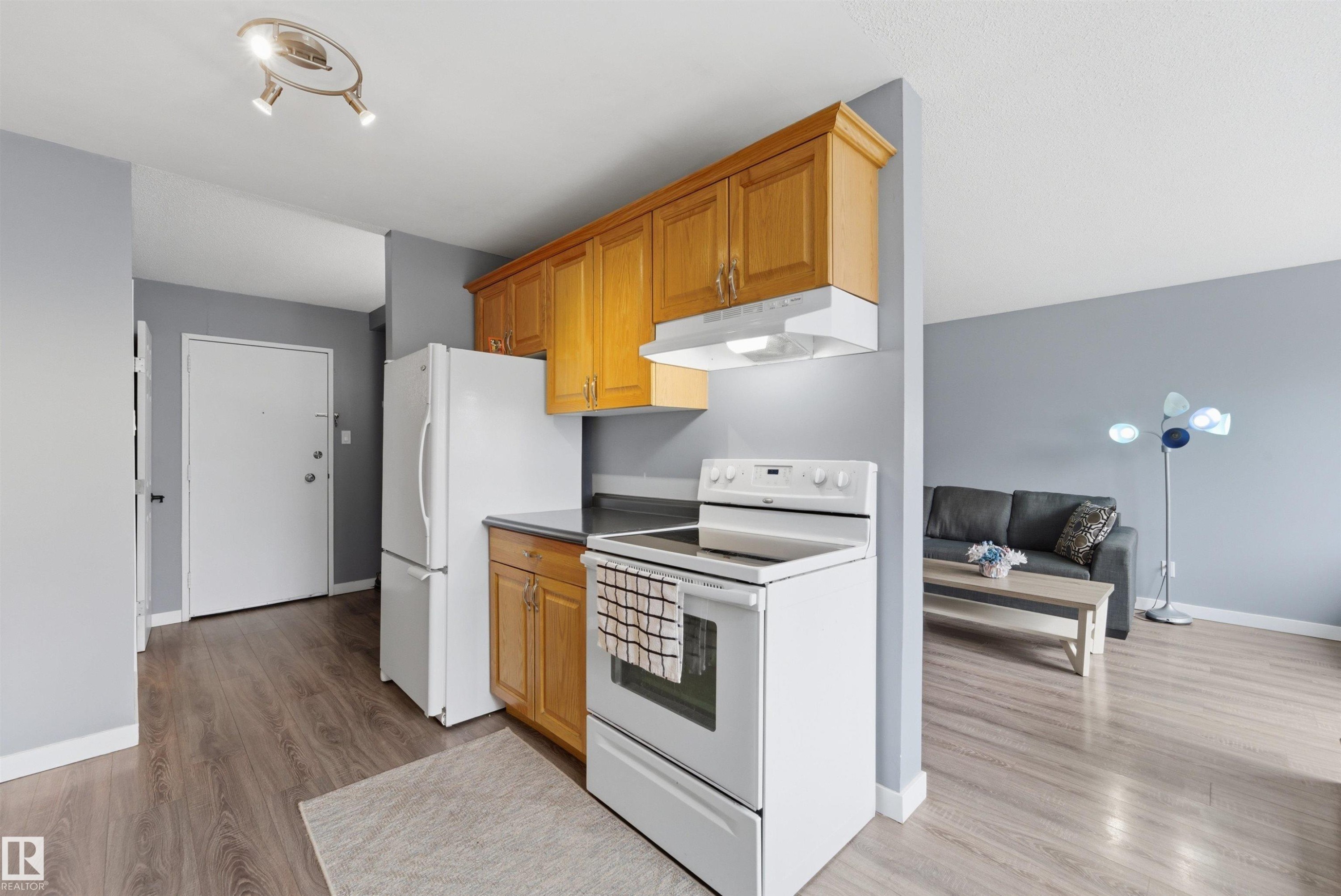 Kitchen area featuring wood cabinetry, white appliances, and dark countertops - #110 7805 159 St Nw, Edmonton, AB