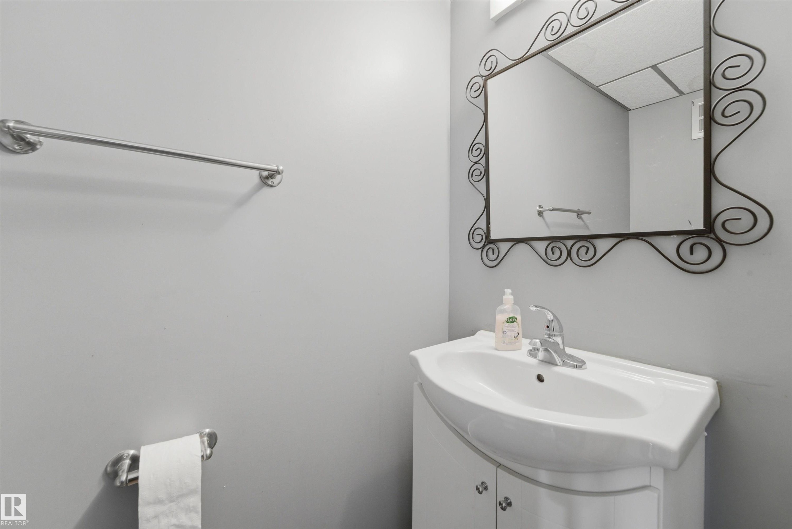 Compact bathroom vanity with integrated white basin, chrome faucet, and a decorative framed mirror - #110 7805 159 St Nw, Edmonton, AB