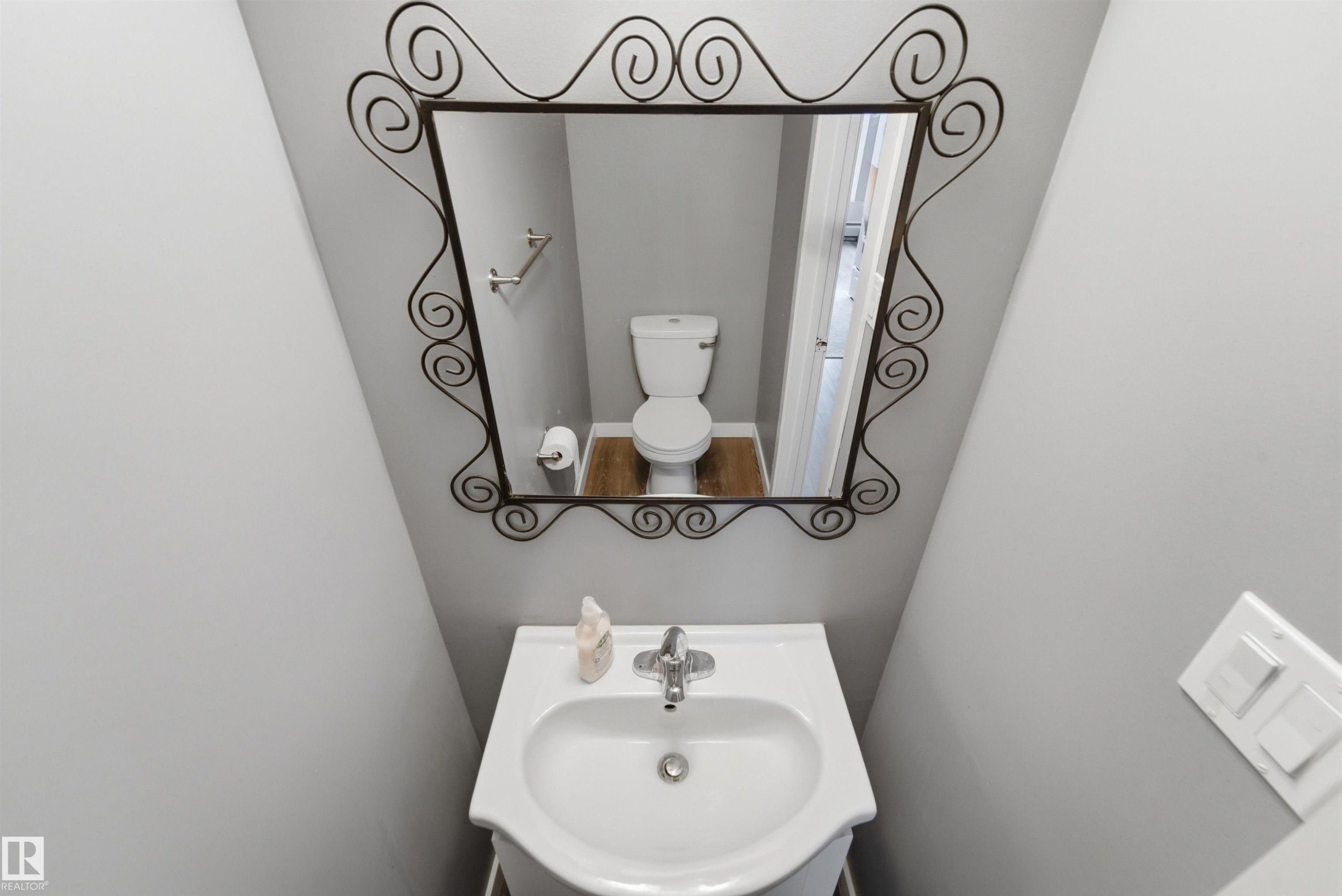 Pedestal sink with chrome faucet, complemented by a decorative iron-framed mirror - #110 7805 159 St Nw, Edmonton, AB