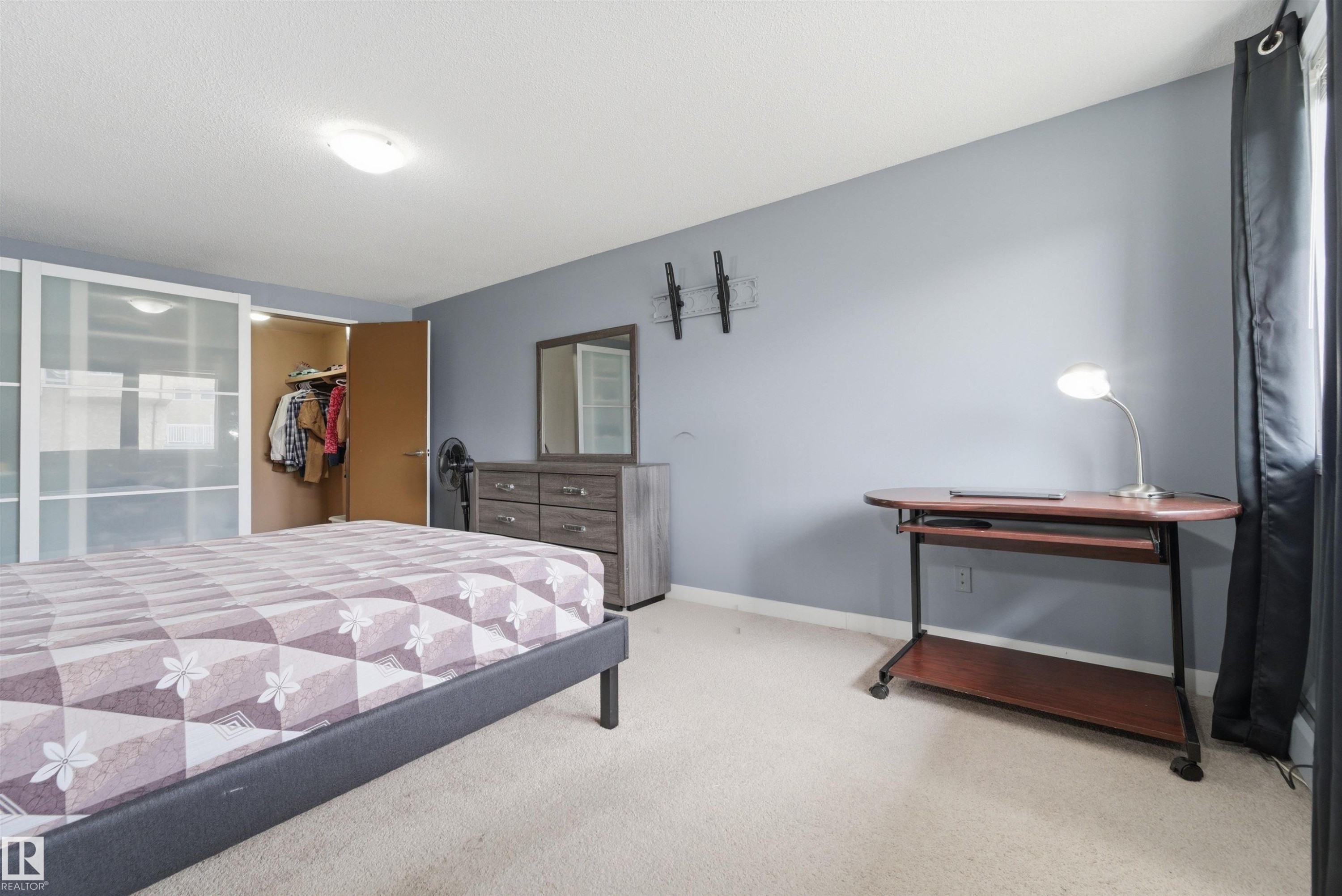 Bedroom featuring light gray walls, carpet flooring, a built-in closet with translucent sliding doors, and a ceiling-mounted light fixture - #110 7805 159 St Nw, Edmonton, AB