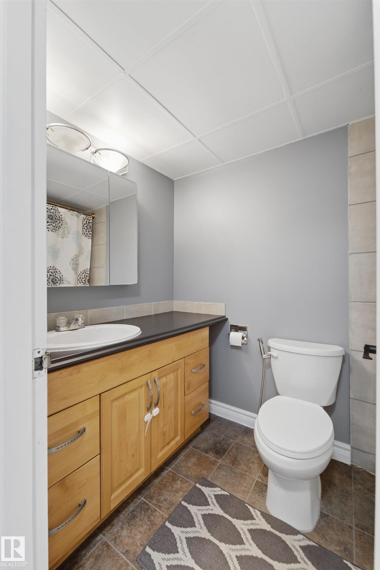 Bathroom featuring a wood-finish vanity with an integrated sink, dark countertop, and tiled flooring - #110 7805 159 St Nw, Edmonton, AB