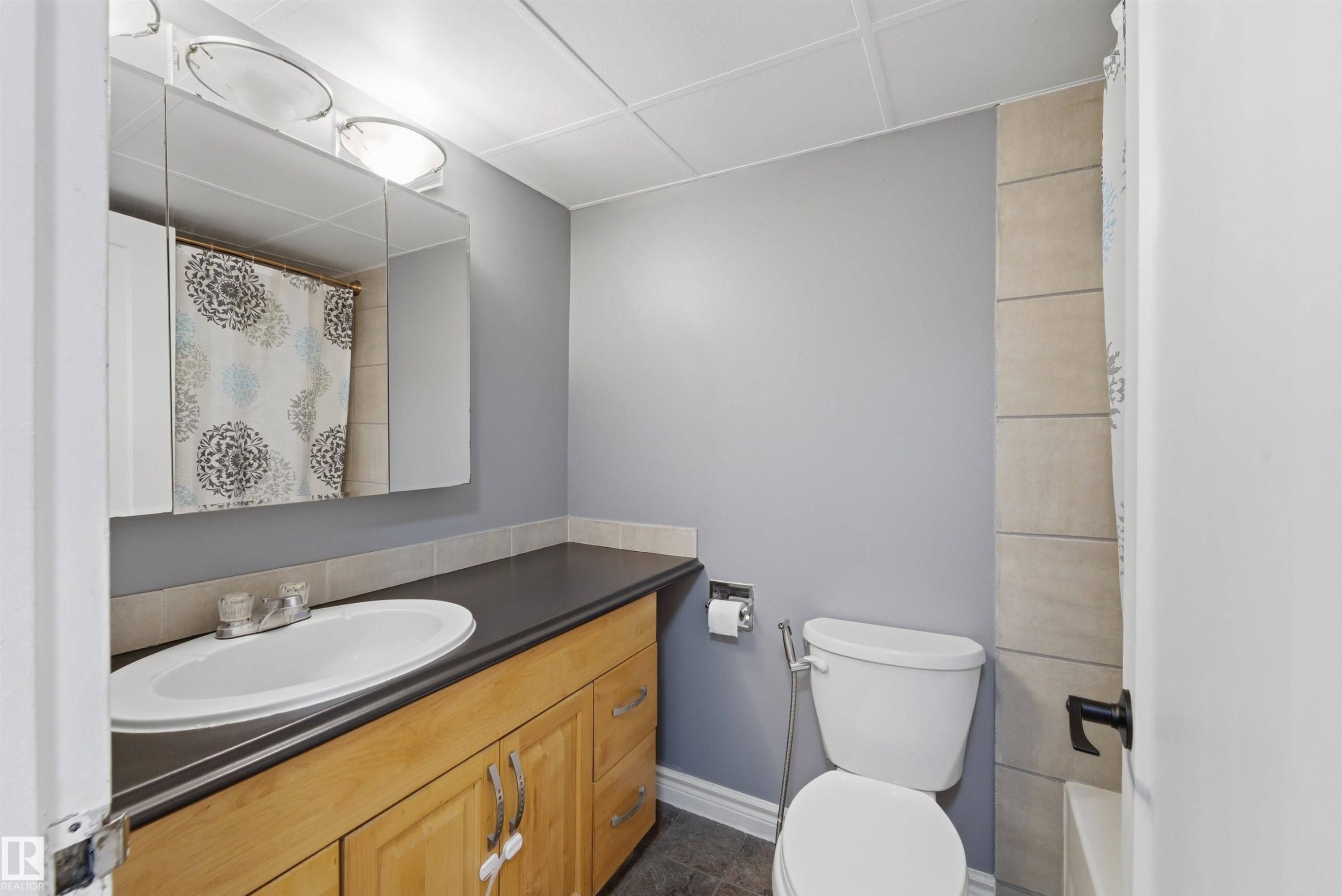 Bathroom featuring a wood-finish vanity with a dark countertop and an undermount sink - #110 7805 159 St Nw, Edmonton, AB