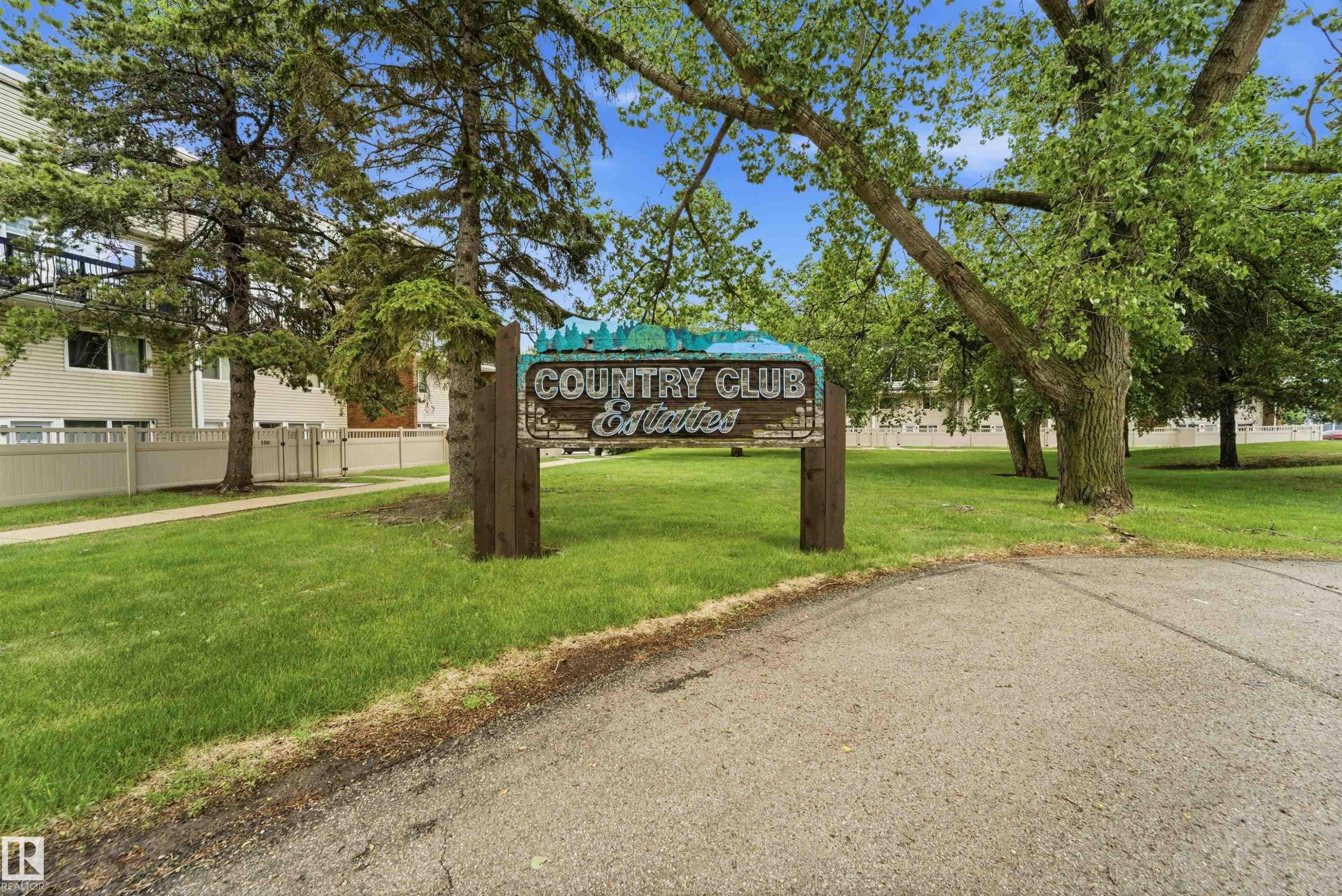"Country Club Estates" entrance sign, set against a backdrop of mature trees and green lawns - #110 7805 159 St Nw, Edmonton, AB