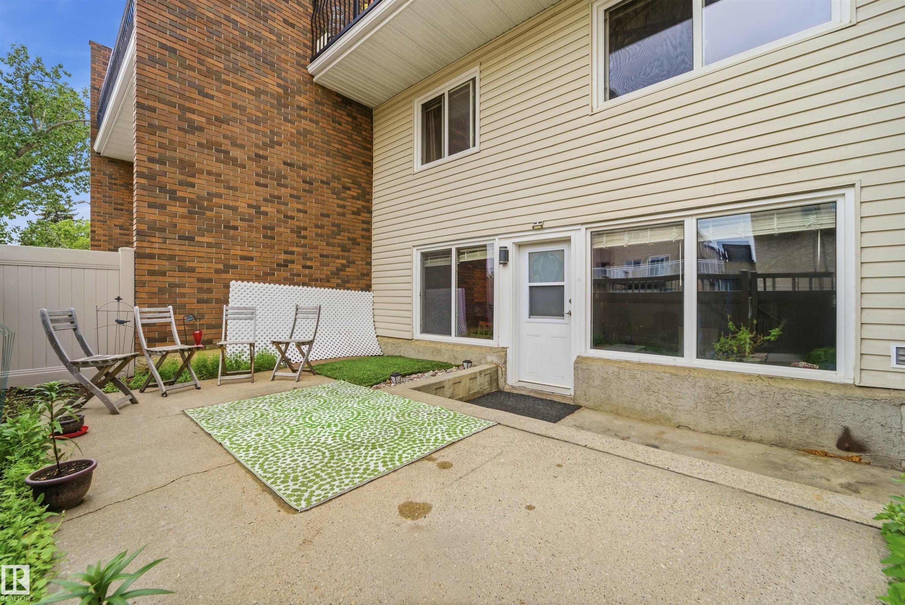 Ground-level patio with a concrete surface, bordered by a white privacy fence and a brick building facade - #110 7805 159 St Nw, Edmonton, AB