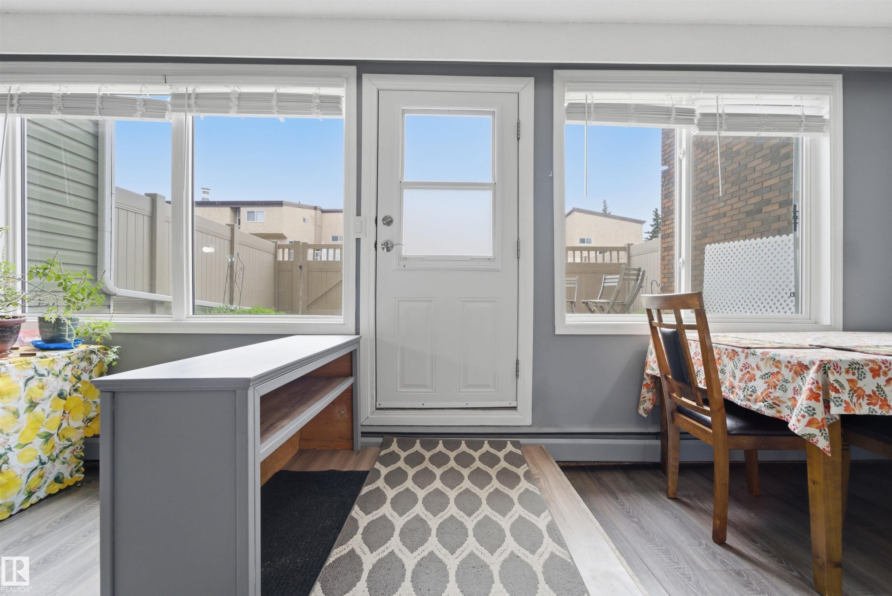 Entryway featuring a white paneled door with three window panels, flanked by two large windows with horizontal blinds, and light wood-finish flooring - #110 7805 159 St Nw, Edmonton, AB