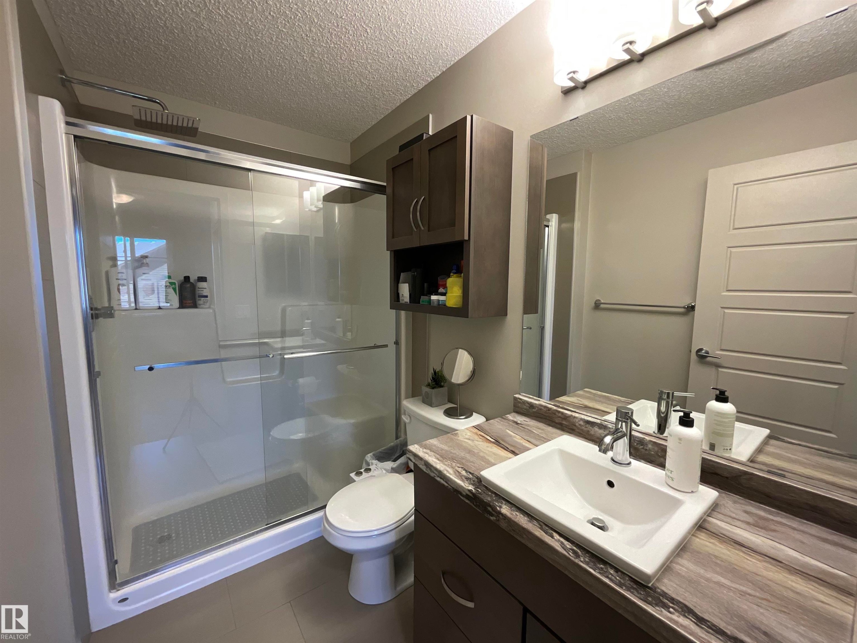 Bathroom featuring a glass-enclosed shower, a vanity with a white rectangular sink, a large mirror, a four-light fixture, and built-in wall cabinetry - 209 1004 Rosenthal Boulevard, Edmonton, AB