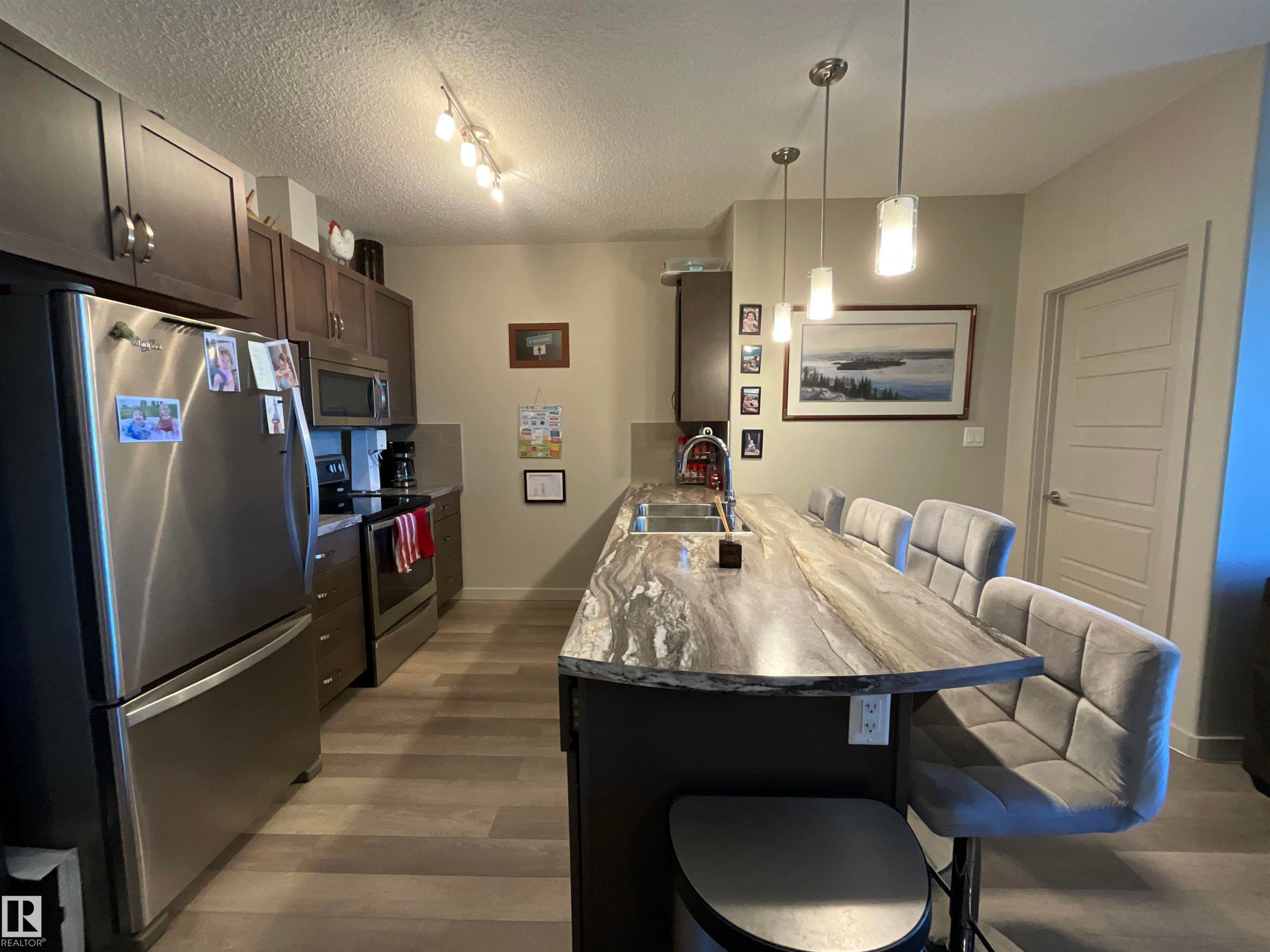 Kitchen featuring wood-finish flooring, dark wood cabinetry, and stainless steel appliances - 209 1004 Rosenthal Boulevard, Edmonton, AB